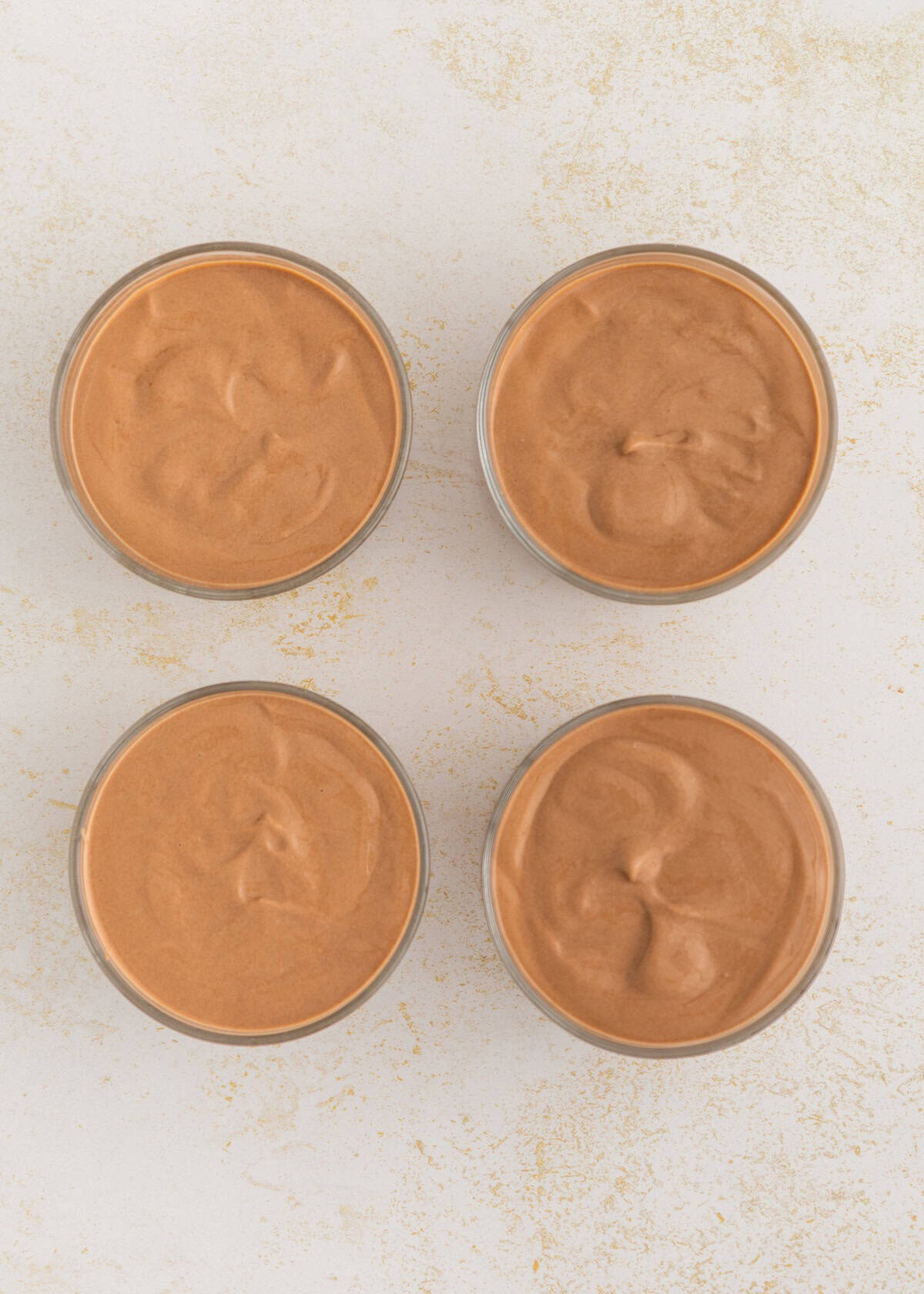 Four glass bowls filled with creamy chocolate mousse on a light, textured surface.