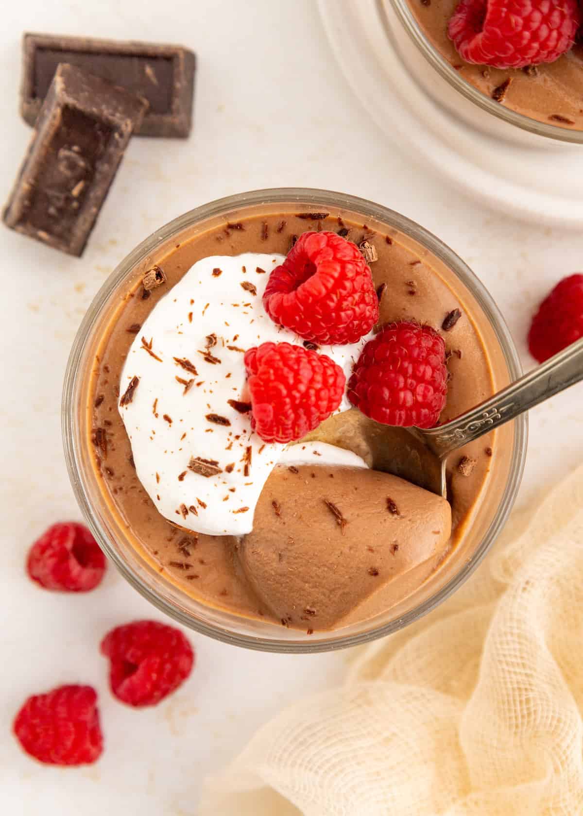 Chocolate mousse topped with whipped cream, raspberries, and chocolate shavings in a glass.