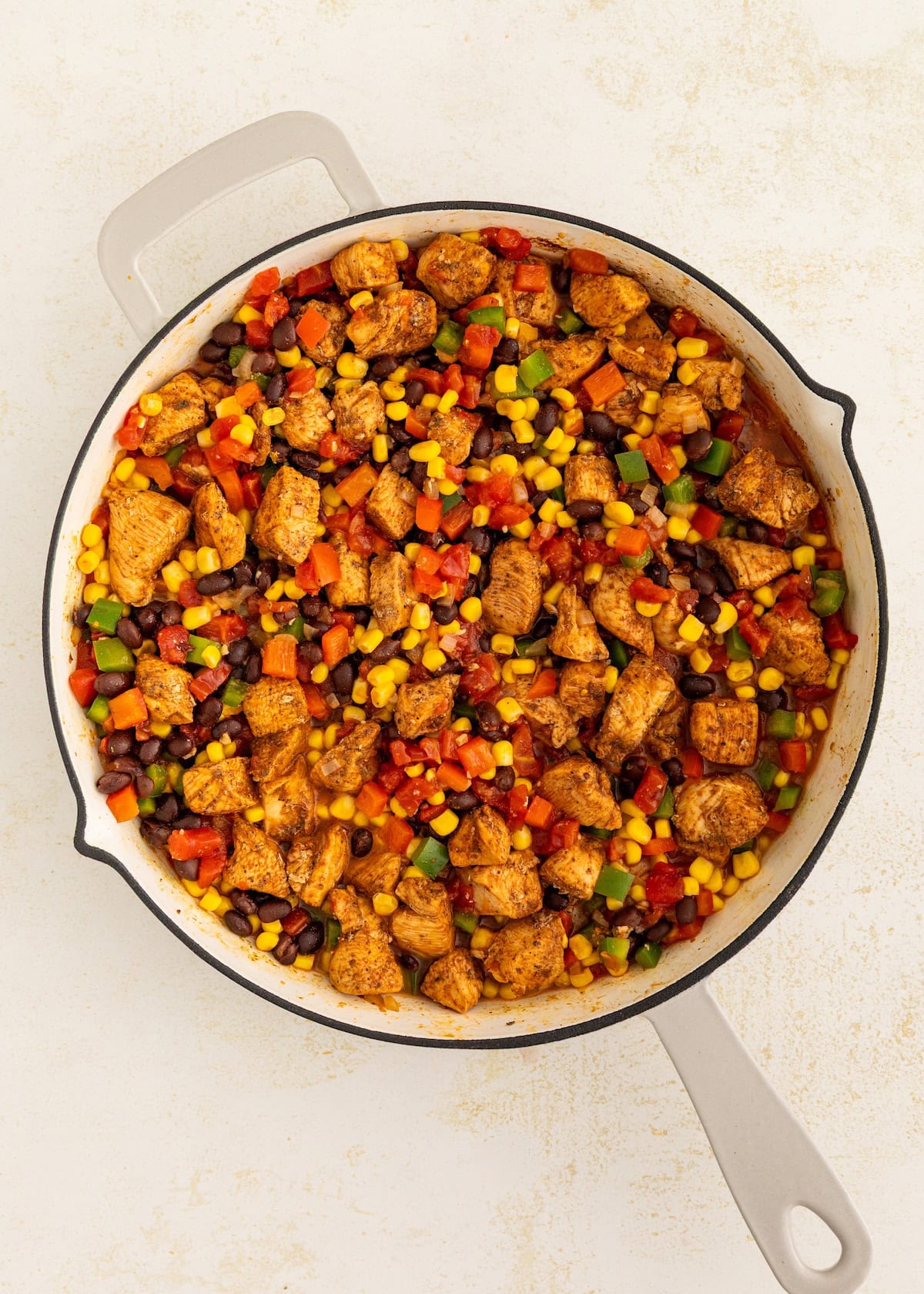 A skillet filled with cooked chicken, corn, black beans, and colorful diced vegetables.