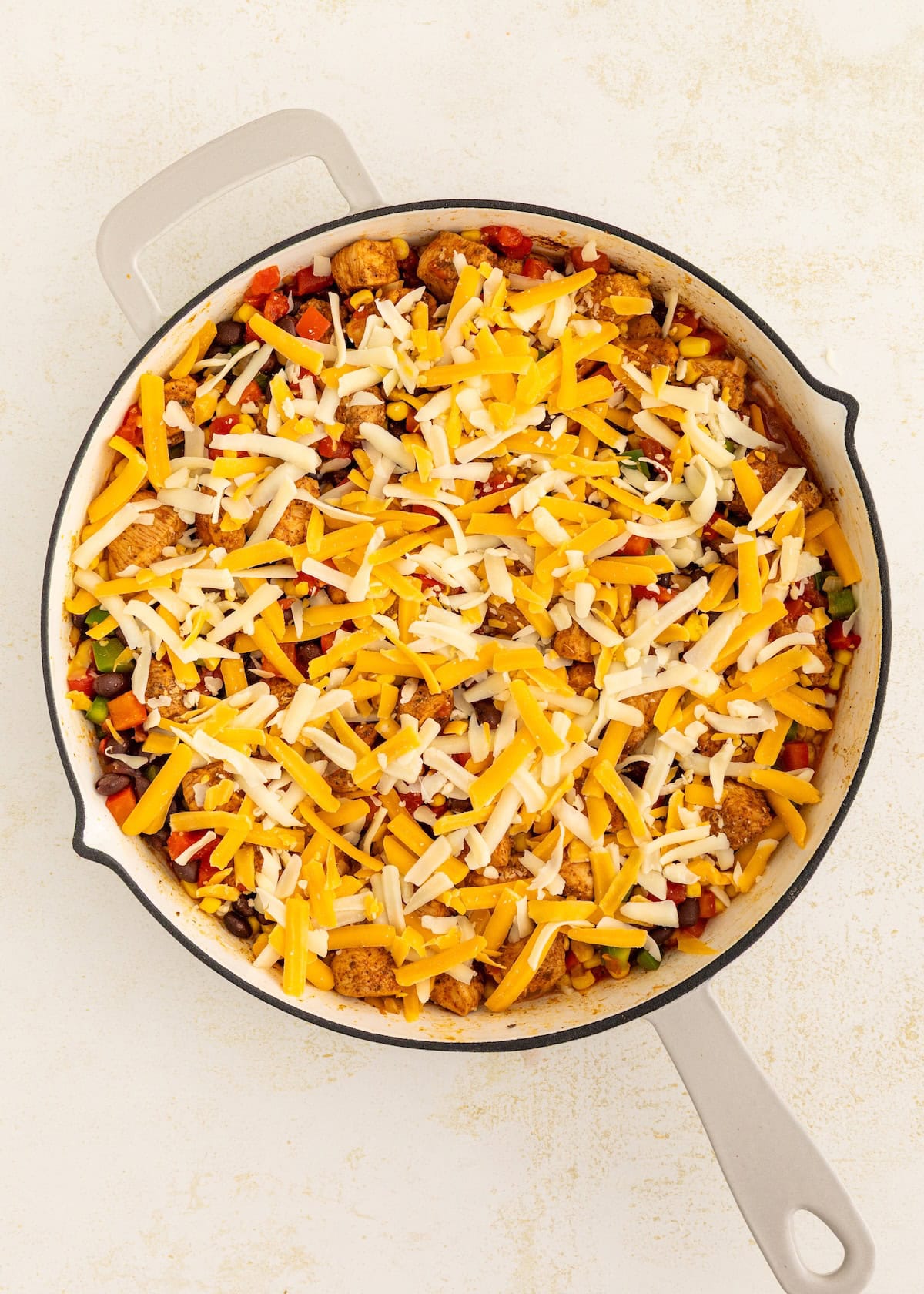 A skillet filled with a colorful dish topped with shredded cheddar and mozzarella cheese.