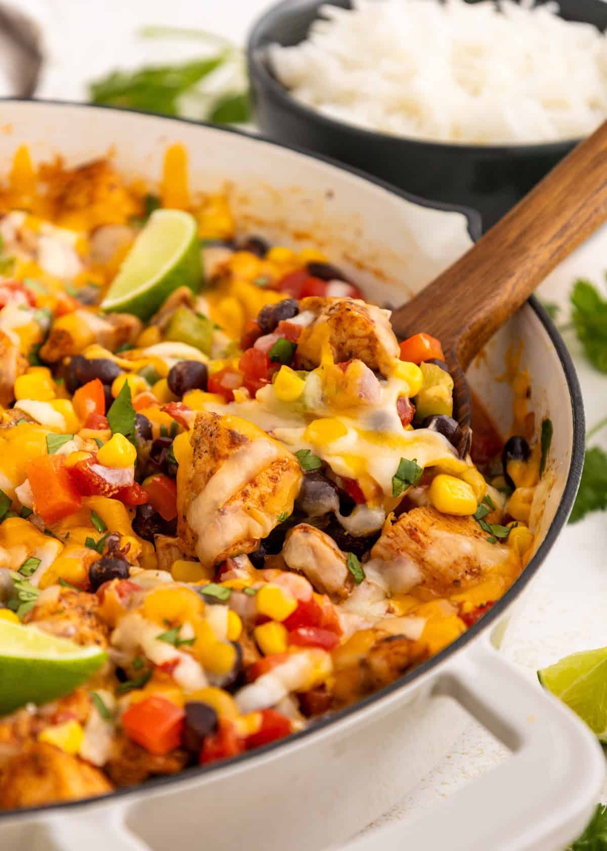 Cheesy chicken, black bean, and corn skillet with veggies, served with rice in the background.