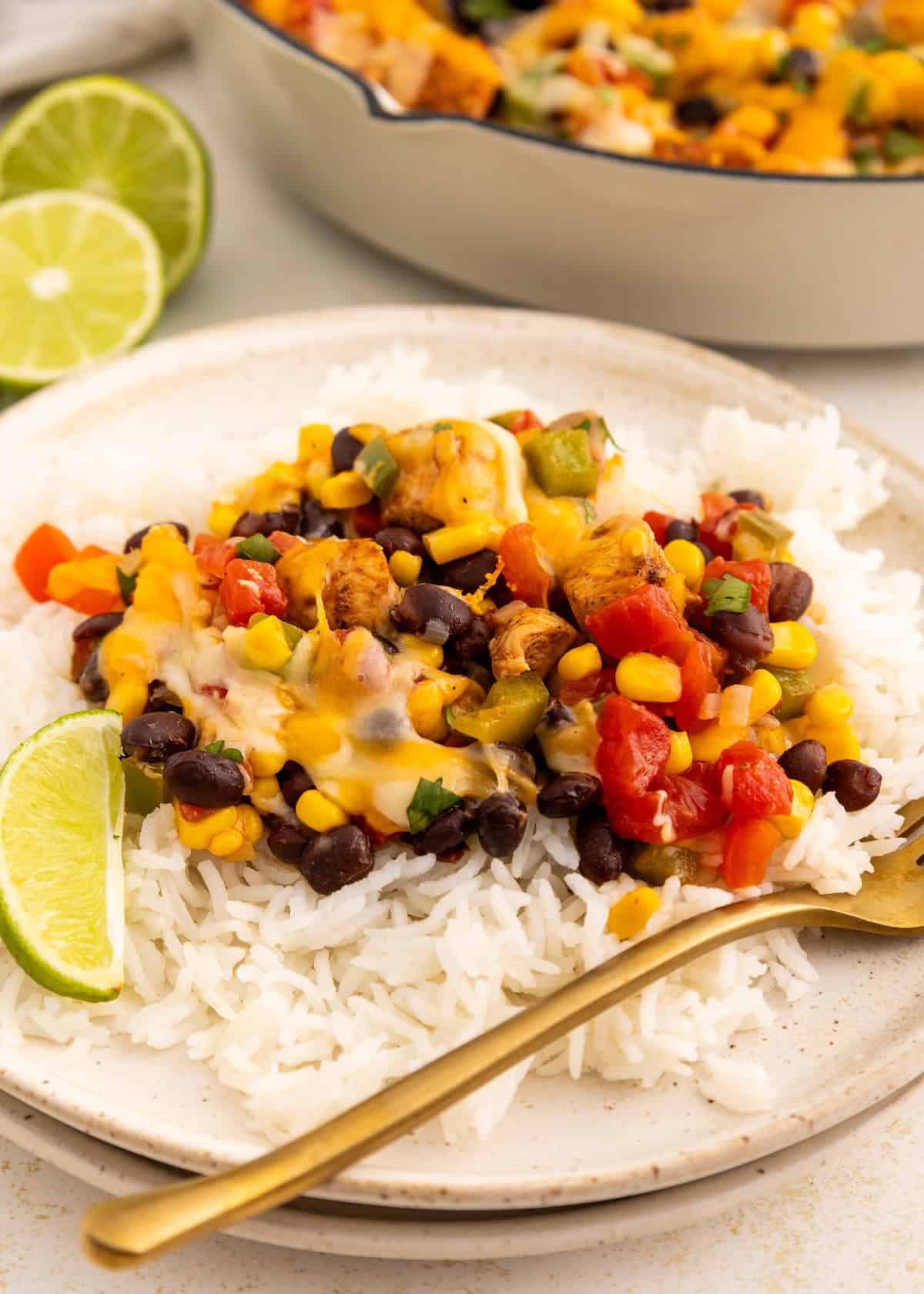 White rice topped with beans, corn, veggies, melted cheese, and a lime wedge on a plate.