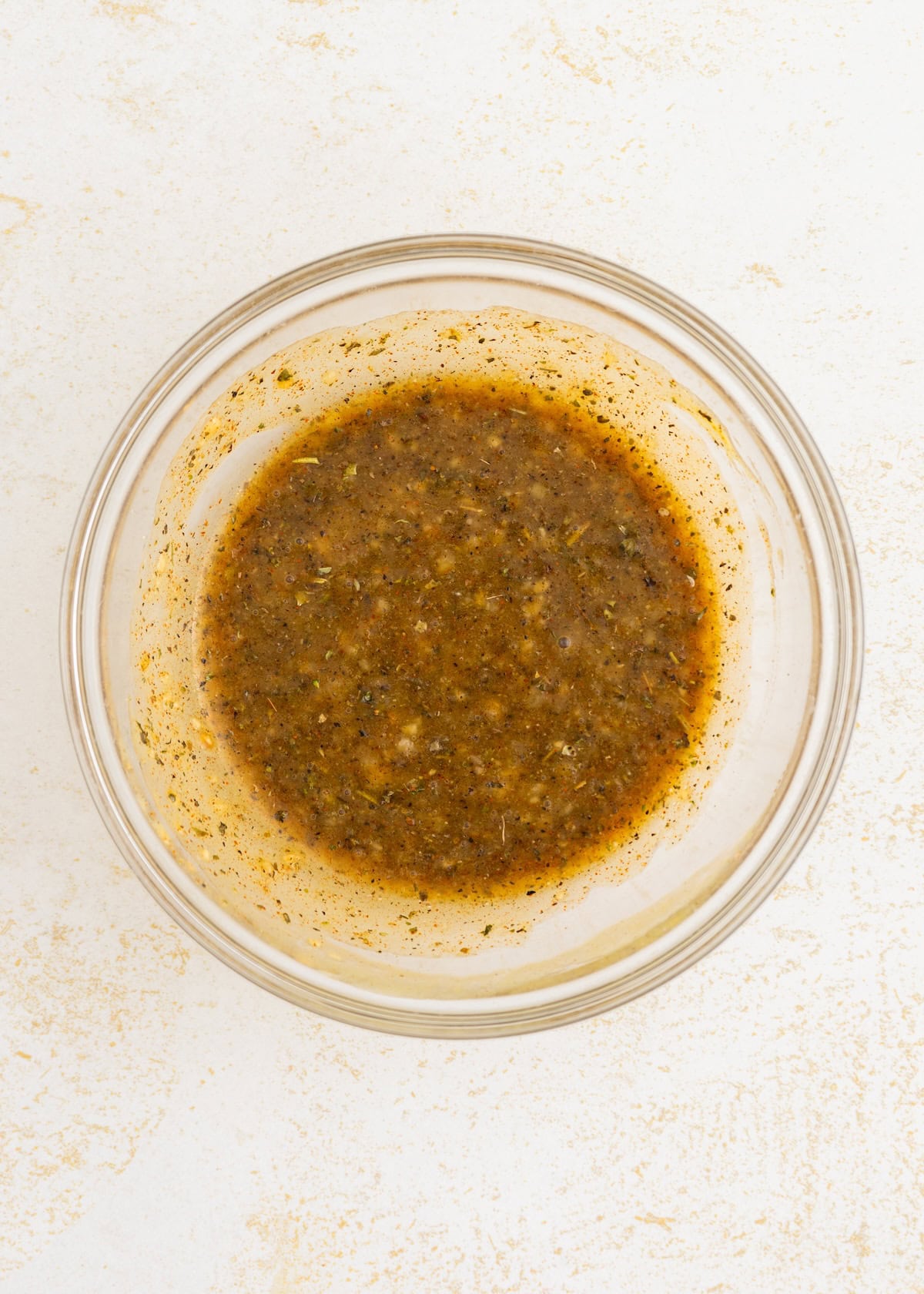 Bowl of mixed seasoning marinade with herbs and spices on a light surface.