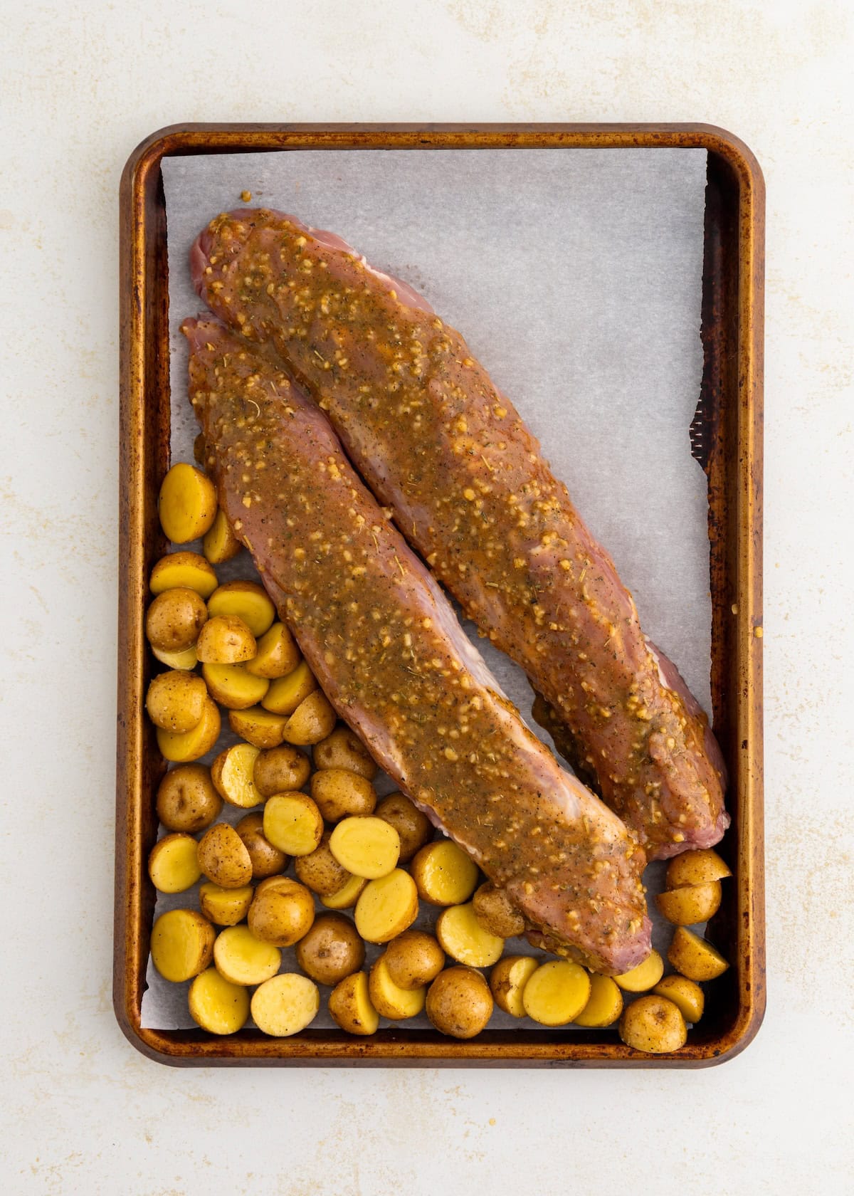 Two seasoned pork tenderloins and sliced potatoes on a baking sheet lined with parchment paper.