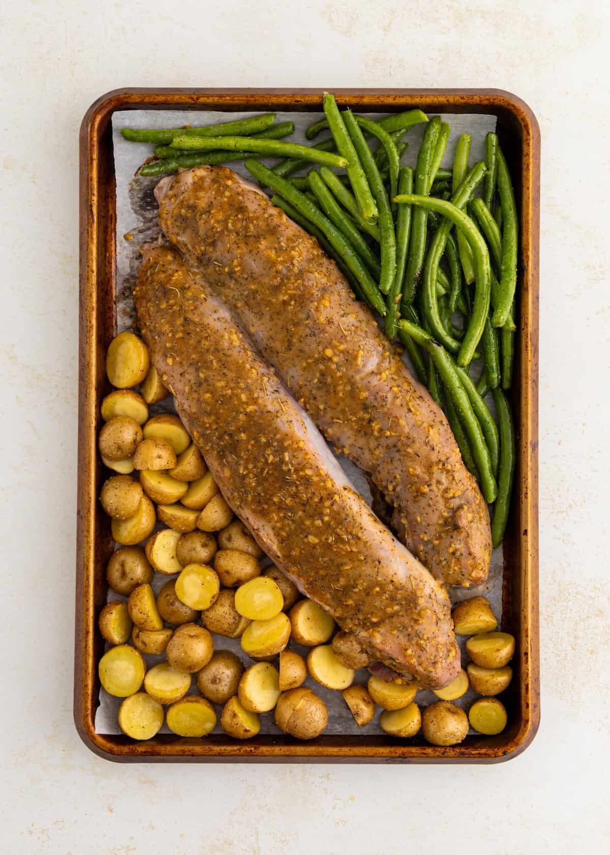 Sheet pan with seasoned pork tenderloin, green beans, and roasted baby potatoes.