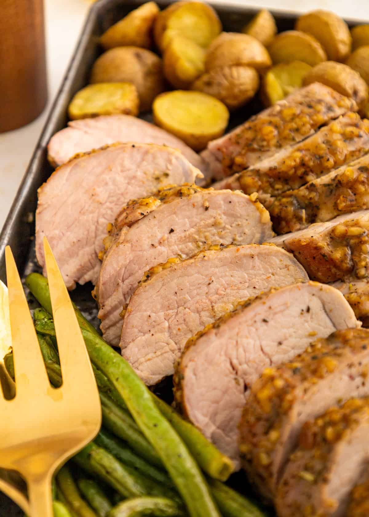 Sliced roasted pork, green beans, and potatoes on a tray with a gold serving fork.