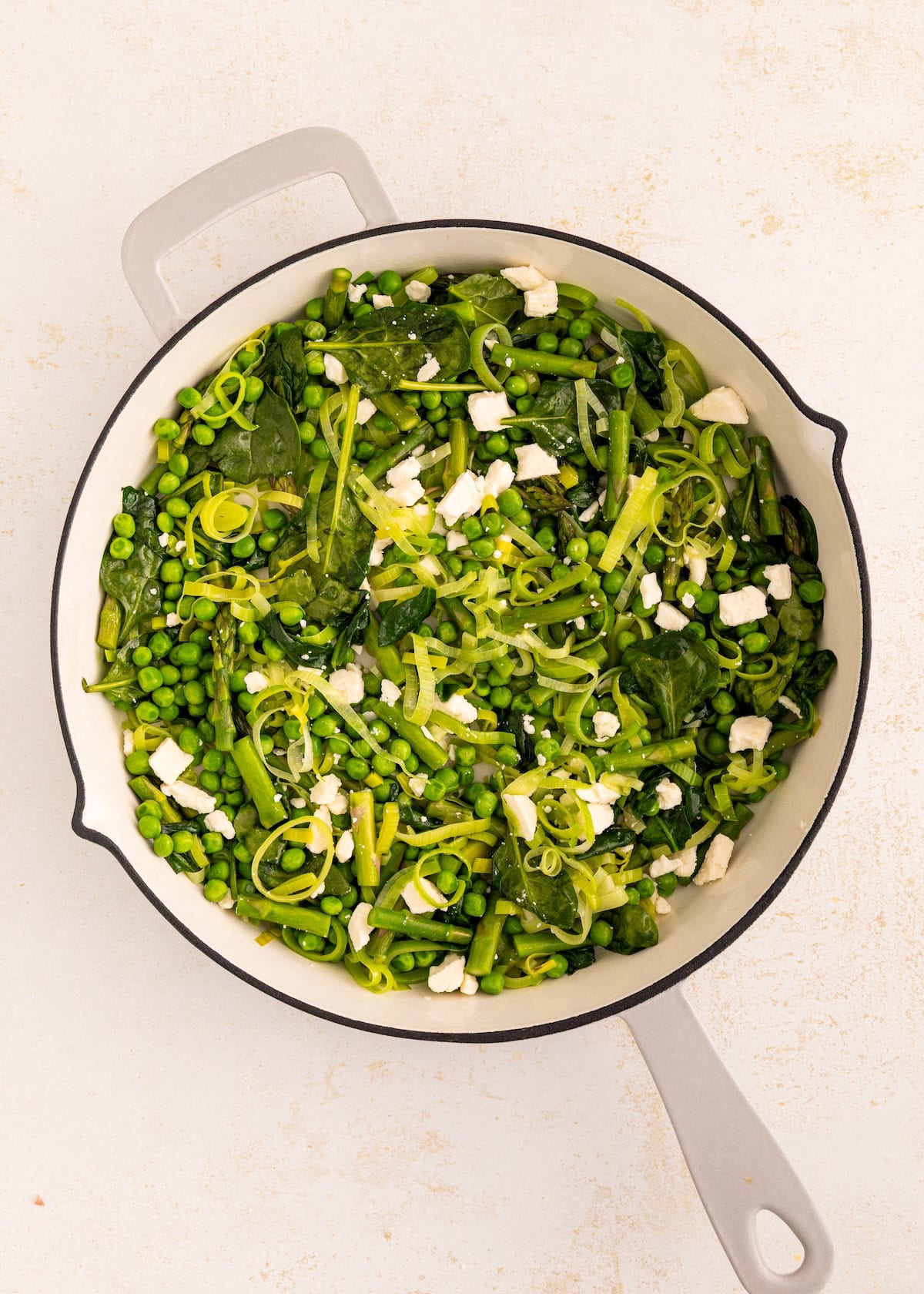 A white pot filled with green vegetables and crumbled cheese on a light background.