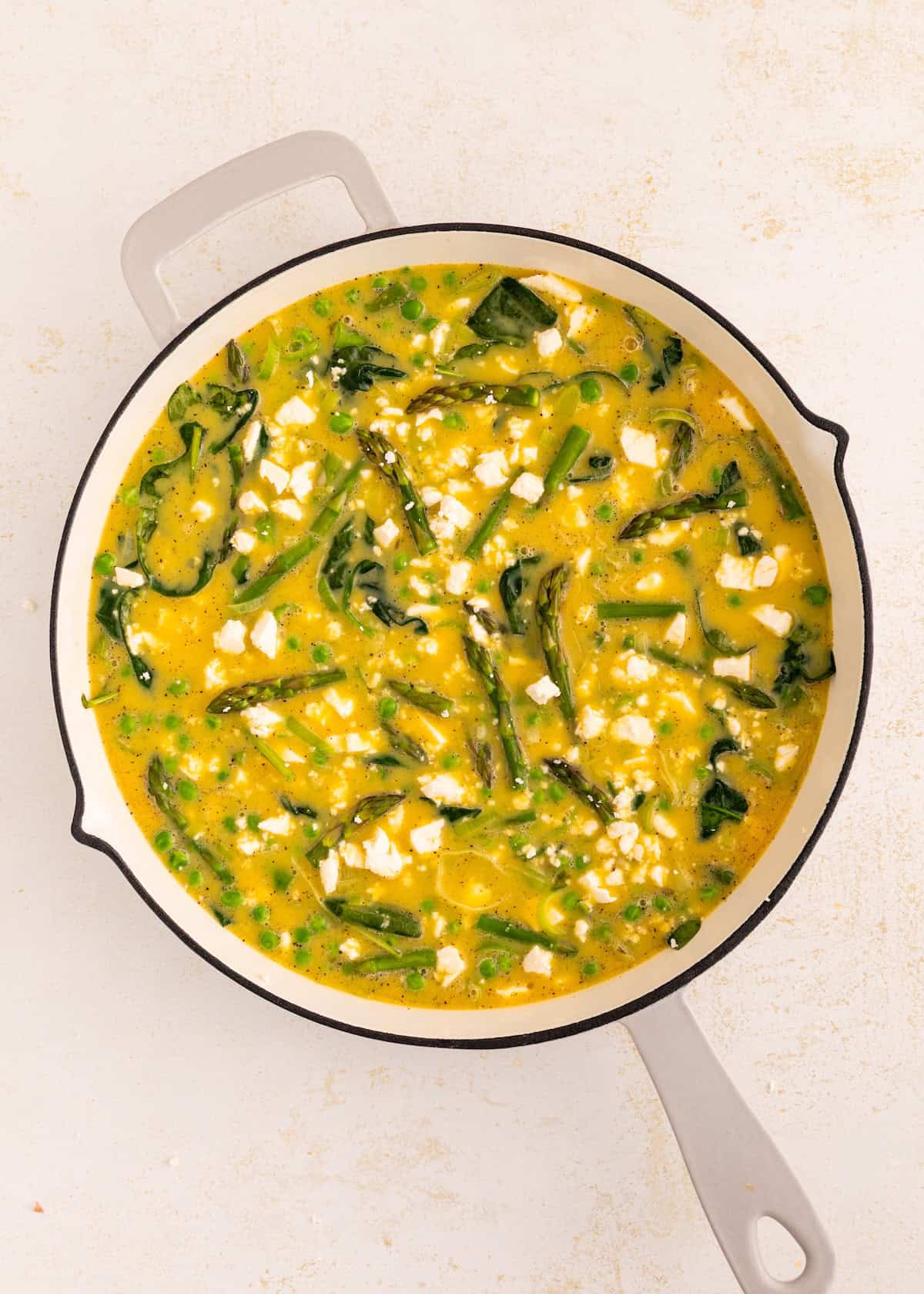 A skillet with a yellow vegetable frittata, topped with greens and crumbled cheese.