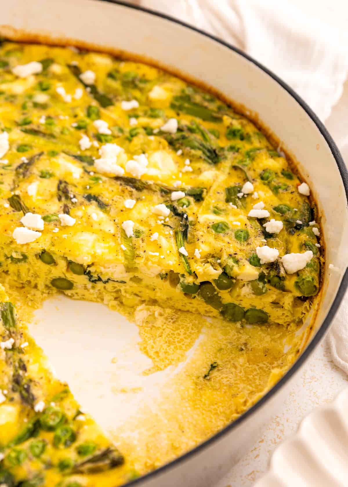 Baked frittata with asparagus and feta cheese, one slice removed from the pan.