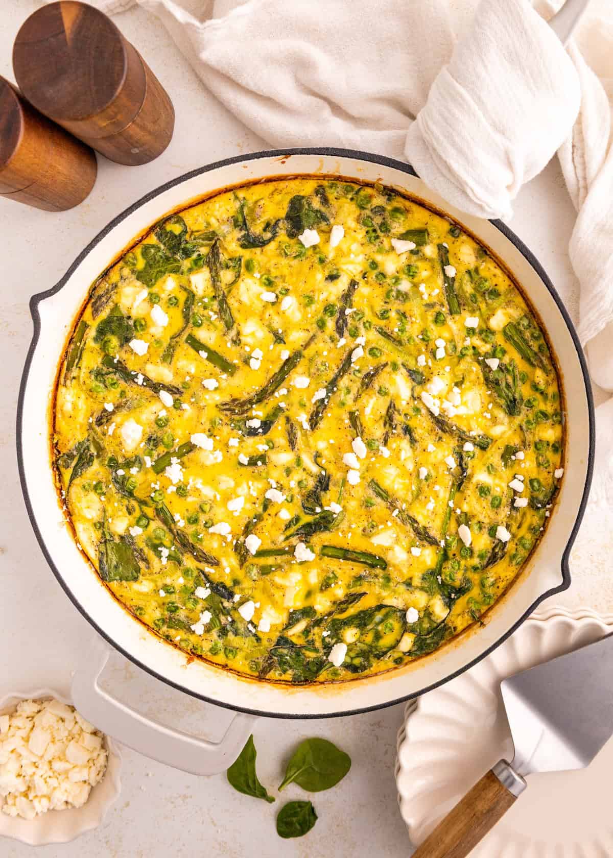 A baked frittata with spinach and feta in a white skillet on a light surface.