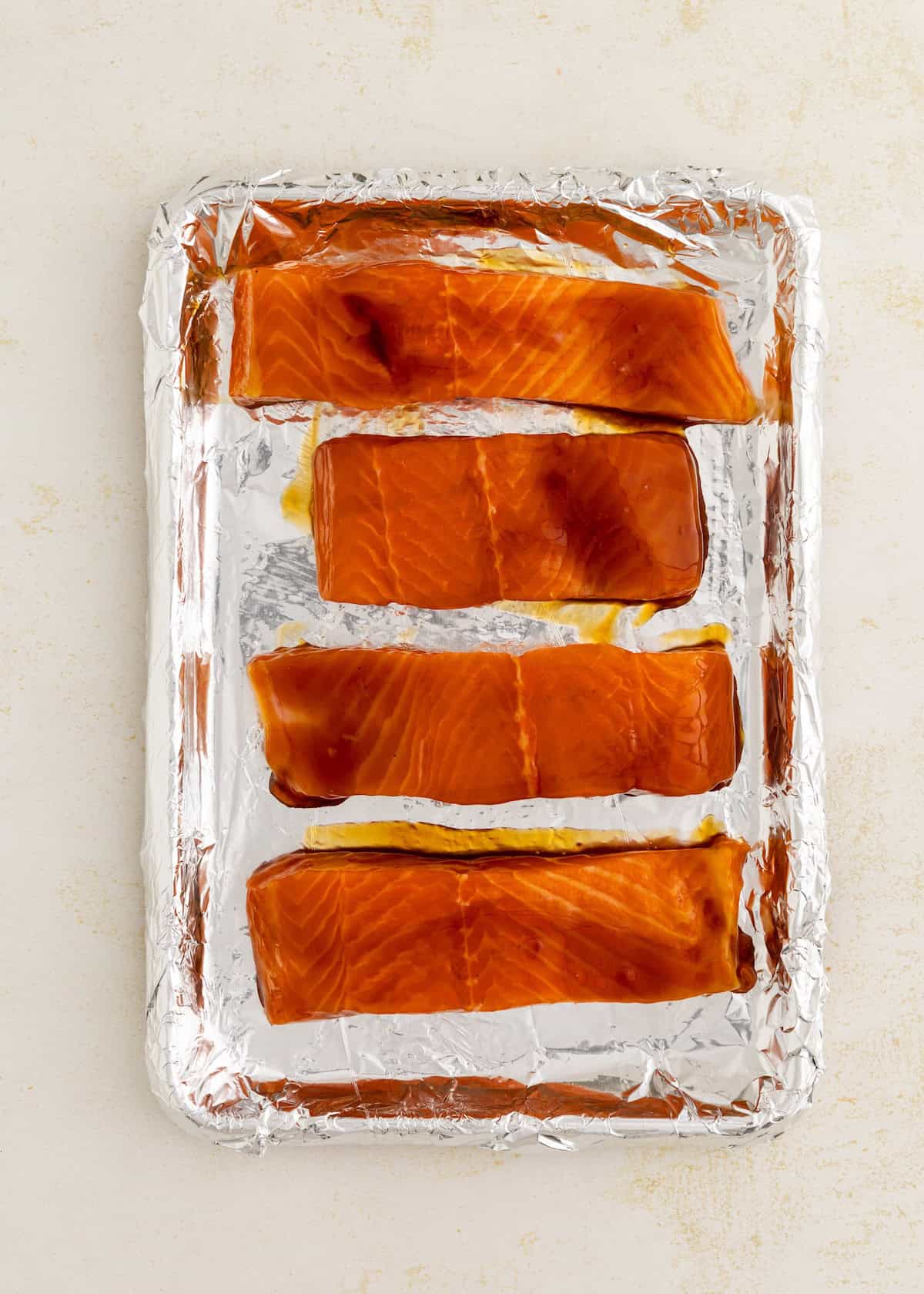Four raw salmon fillets on a foil-lined baking sheet, ready to be cooked.