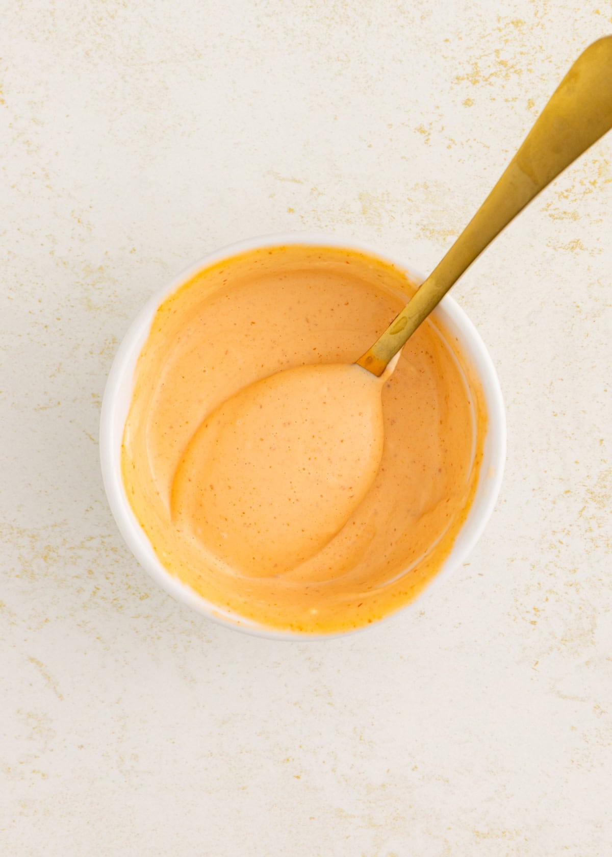 A bowl of creamy orange sauce with a golden spoon on a light surface.