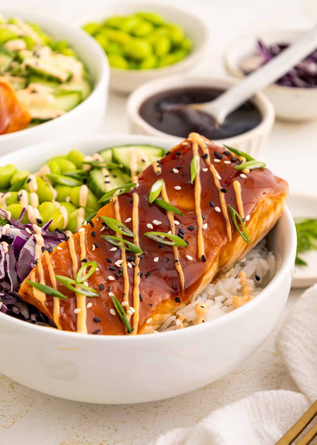 Bowl of rice topped with glazed salmon, sliced veggies, and drizzle of sauce.