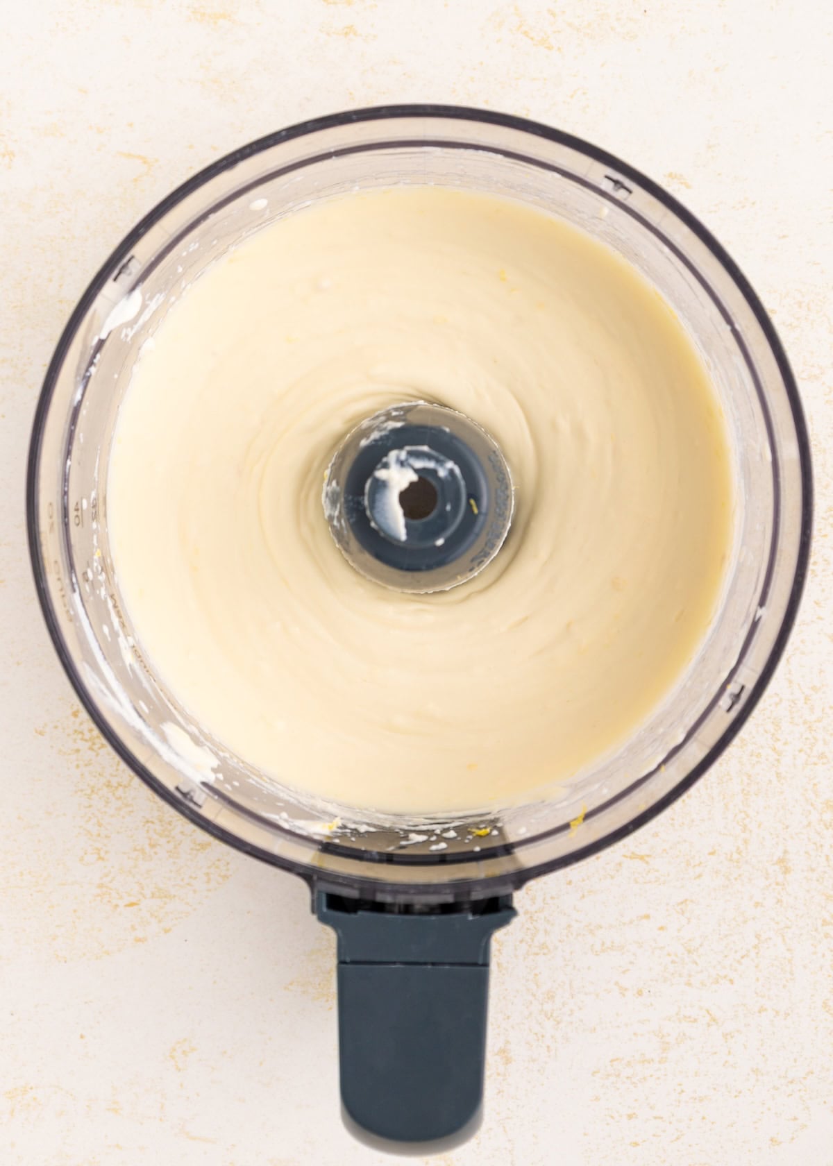 Top view of creamy batter blending in a food processor on a light surface.
