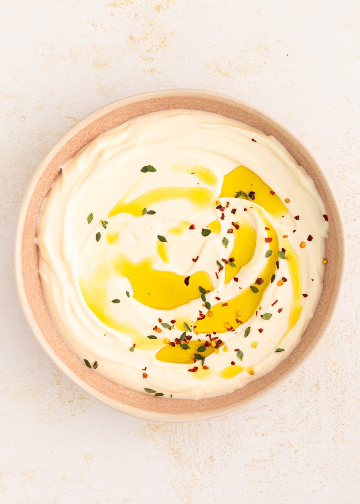 Creamy yogurt topped with olive oil, herbs, and red pepper flakes in a pink bowl.