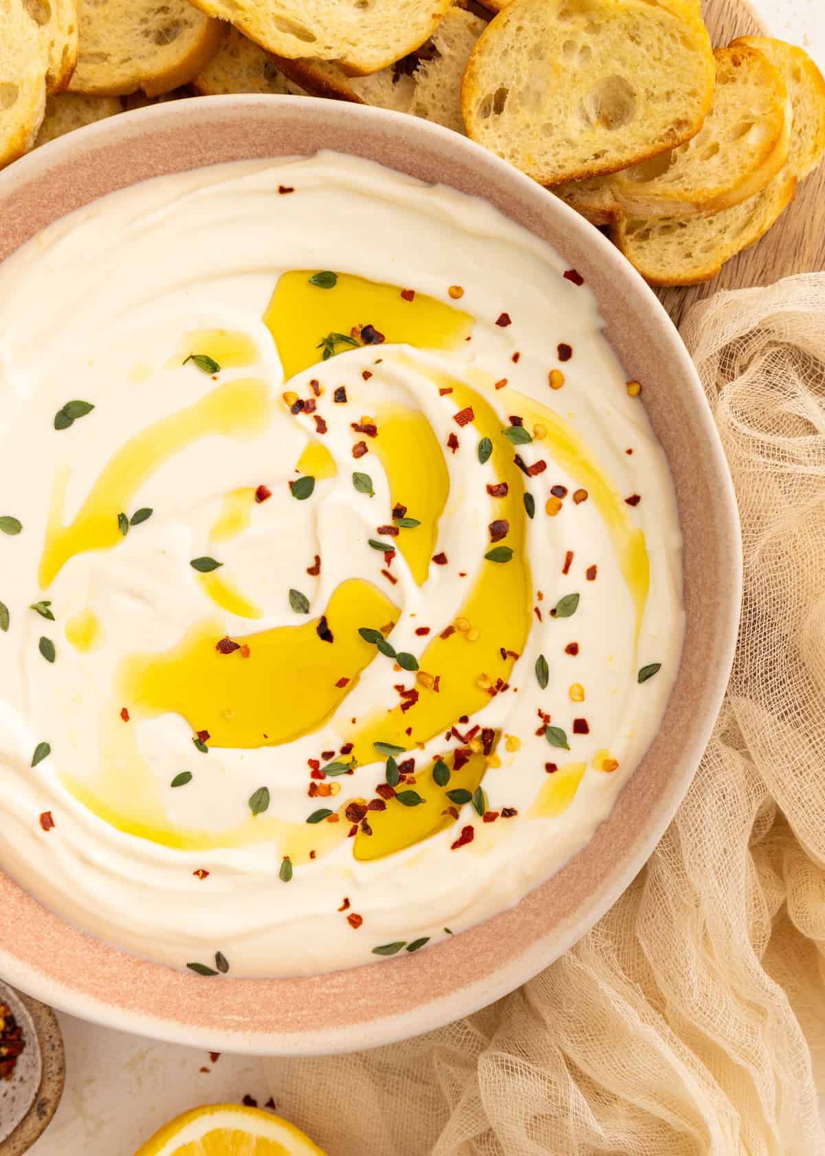 Creamy dip topped with olive oil, herbs, and chili flakes, served with sliced bread.