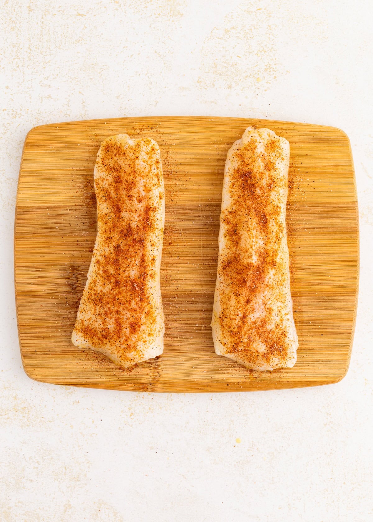 Air fryer cod fillets, seasoned and ready on a wooden cutting board.