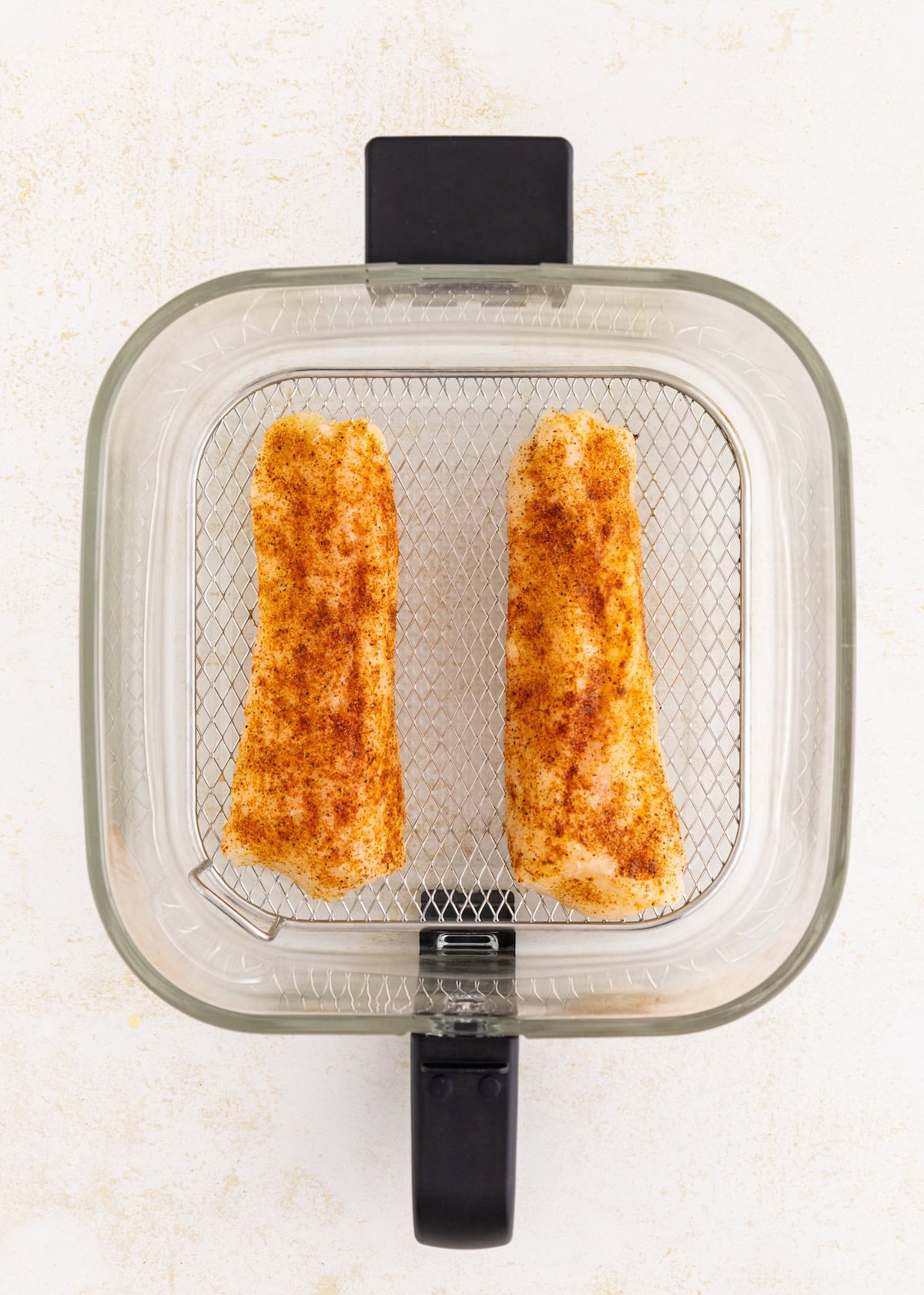 Two seasoned air fryer cod fillets in a basket, ready to be cooked.