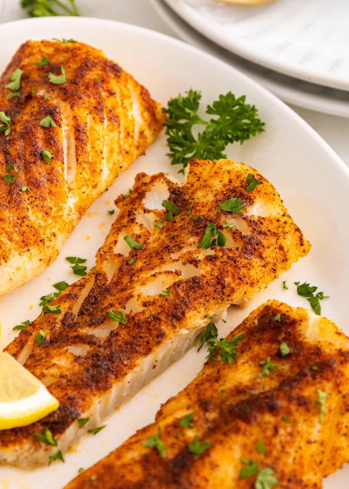 Three pieces of air fryer cod fillet, seasoned and garnished with parsley and a lemon wedge.