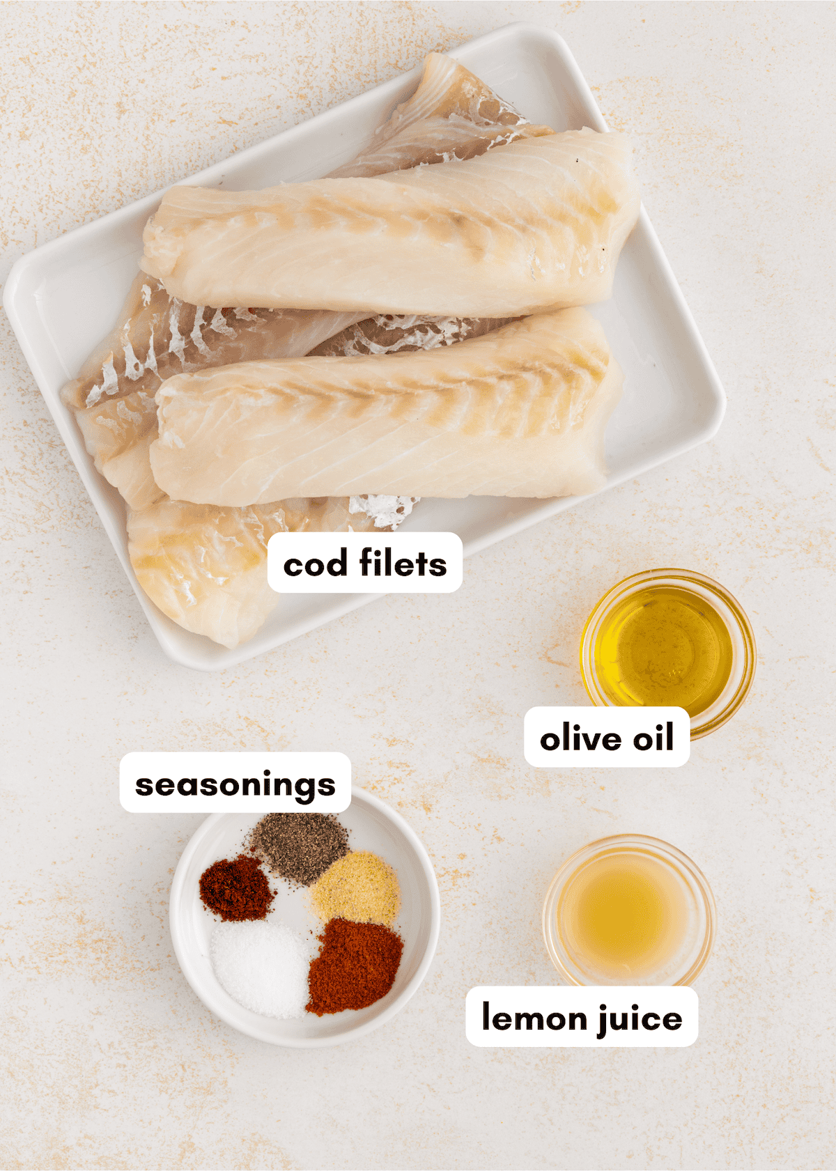 Air fryer cod filets, olive oil, lemon juice, and seasonings on a light surface.