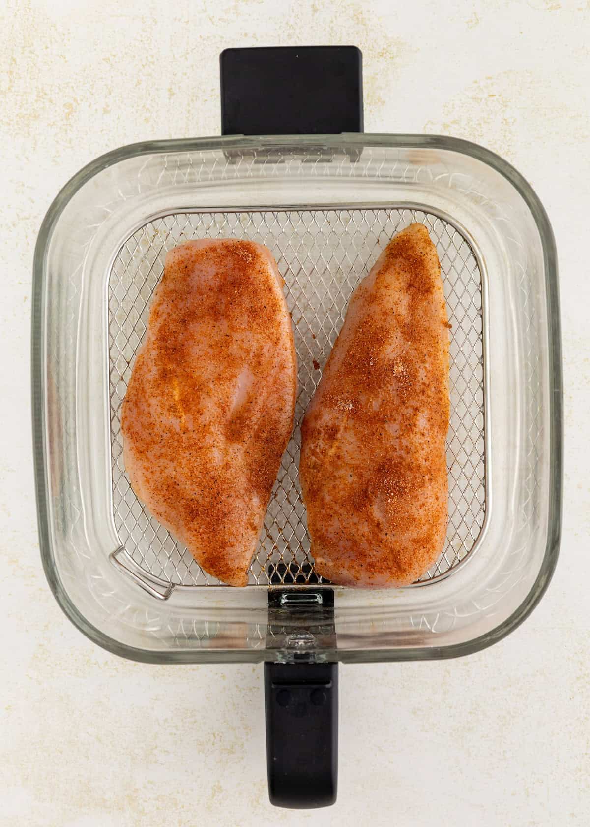 Two seasoned Air Fryer Grilled Chicken breasts in a basket, ready to be cooked.
