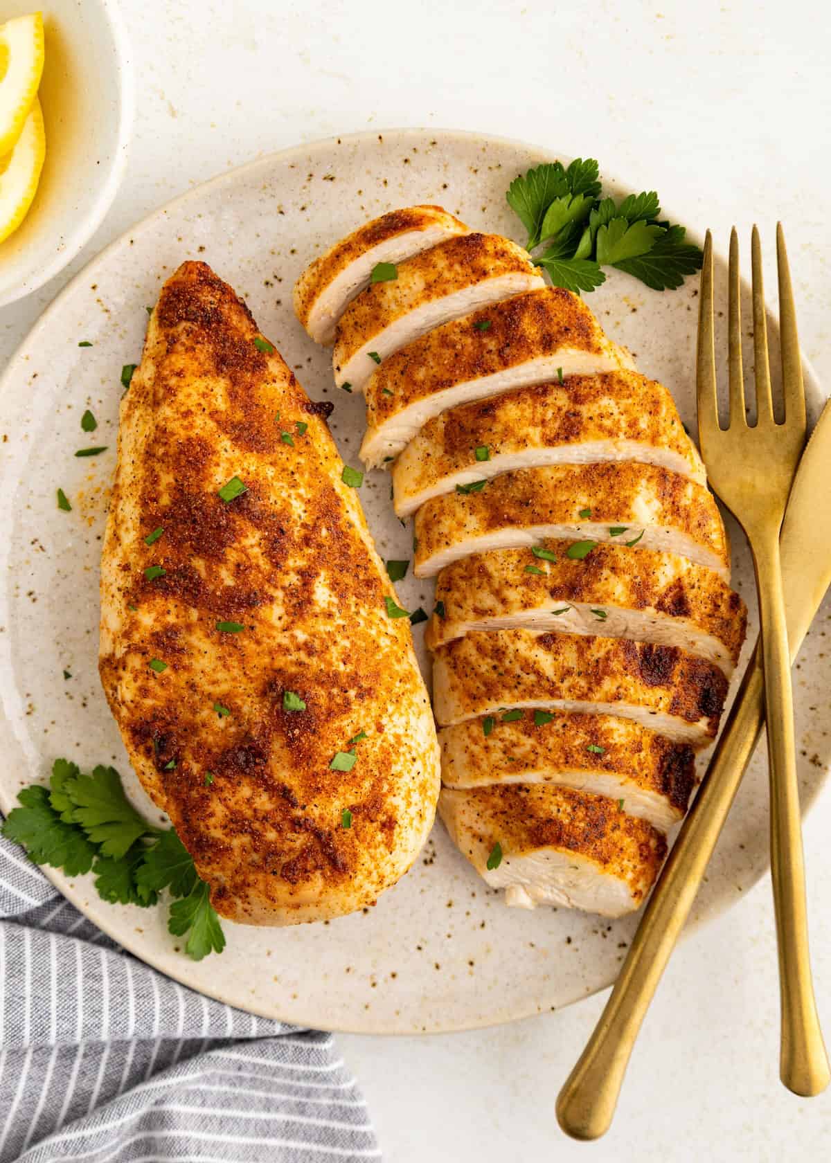 Air Fryer Grilled Chicken breasts, one whole and one sliced, served with parsley and cutlery.