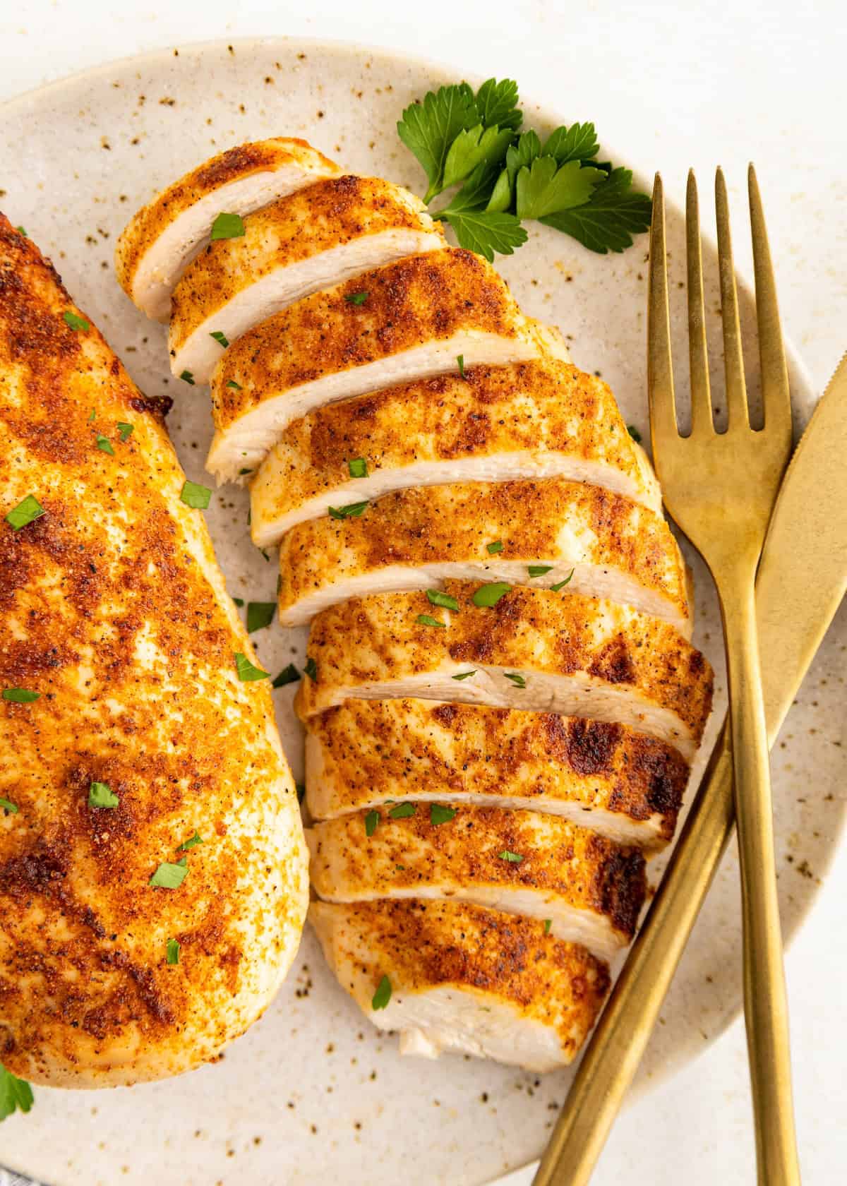 Air Fryer Grilled Chicken breast, sliced and seasoned, served with herbs, fork, and knife.