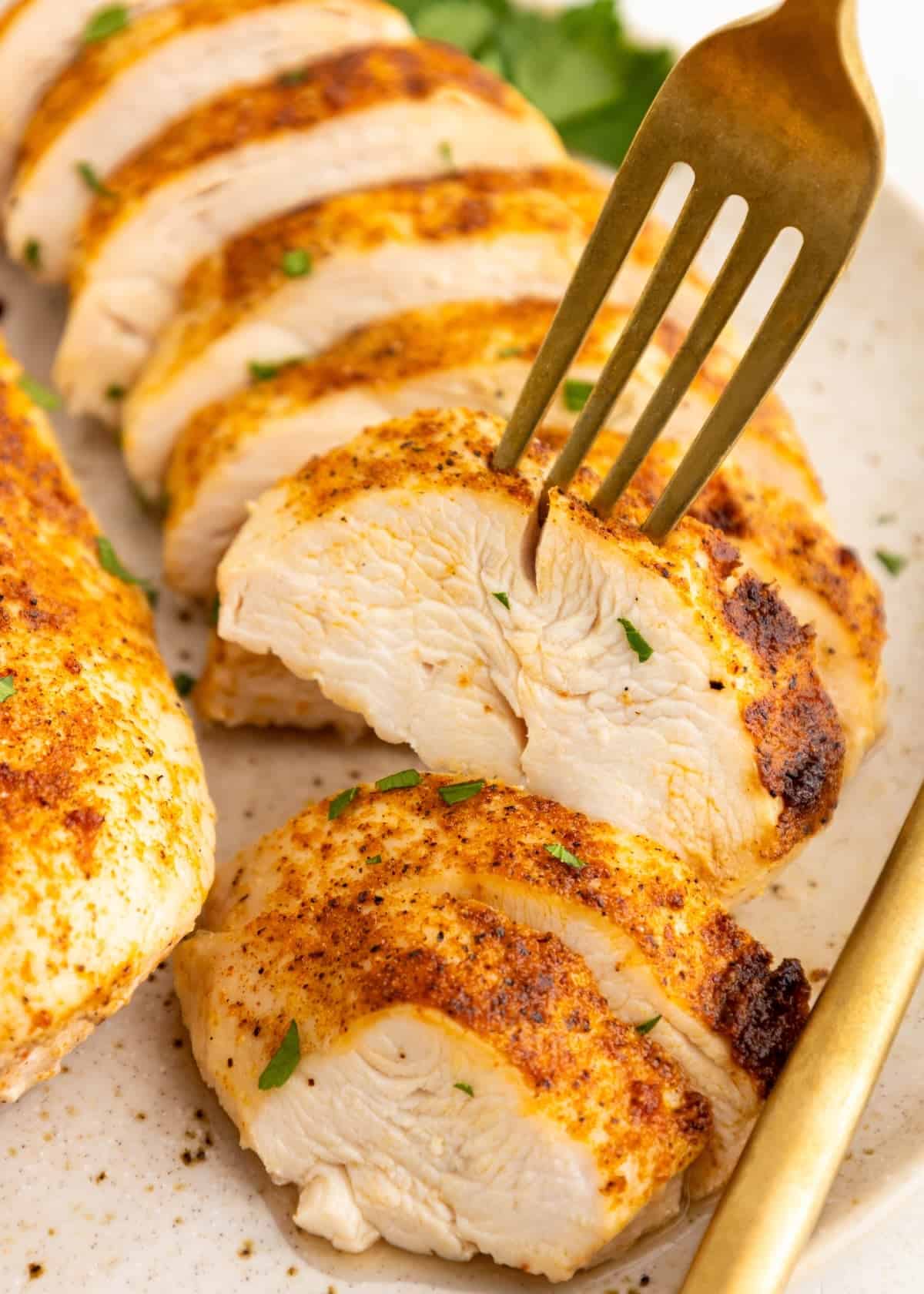 Air Fryer Grilled Chicken breast, sliced and seasoned, served on a plate with a gold fork.