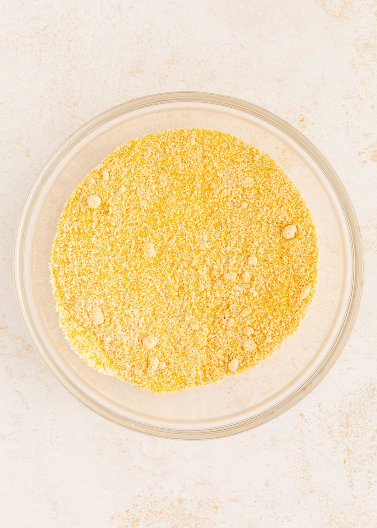 A glass bowl filled with yellow cornmeal on a light-colored surface.