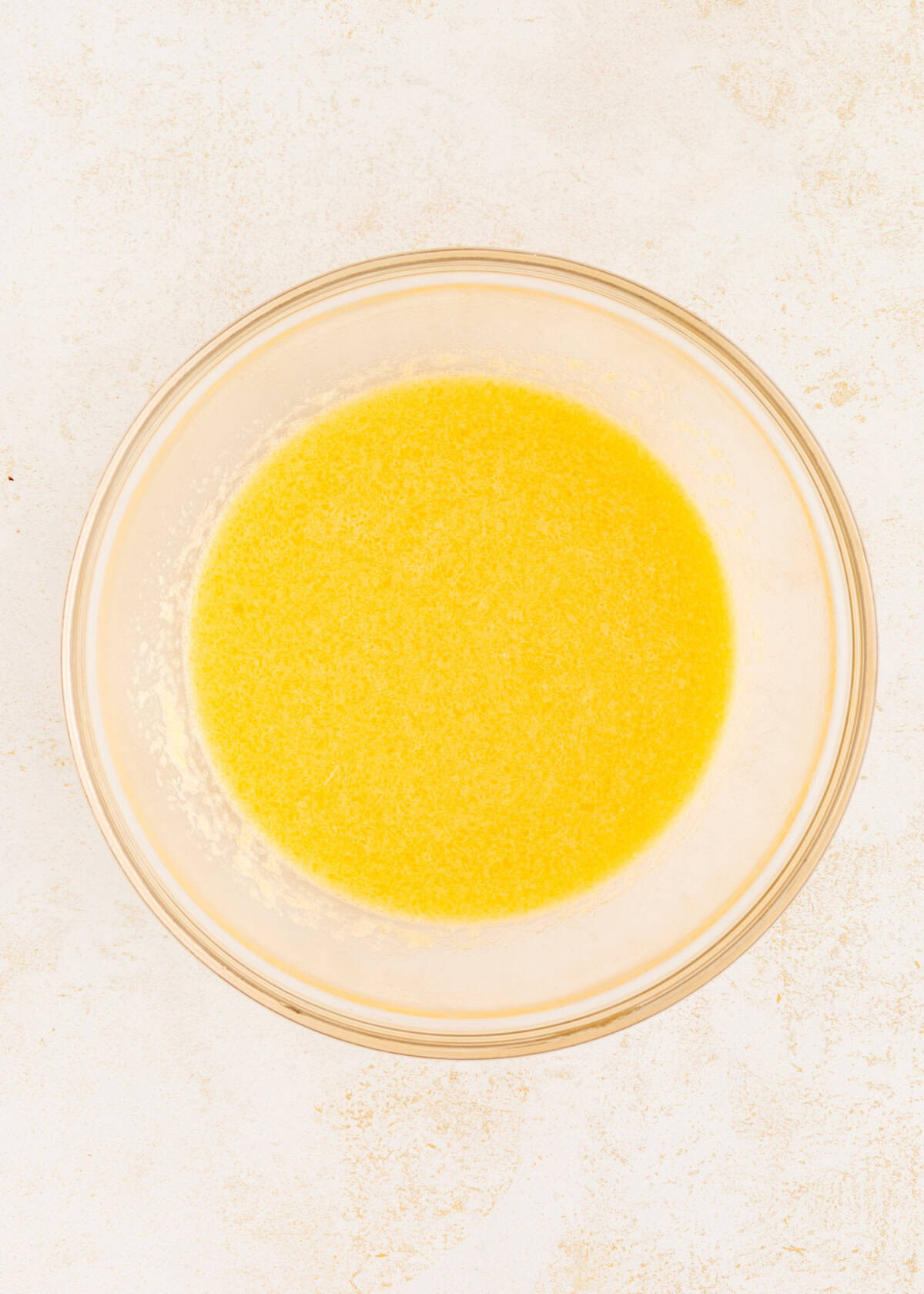 A glass bowl filled with melted butter on a light, textured surface.