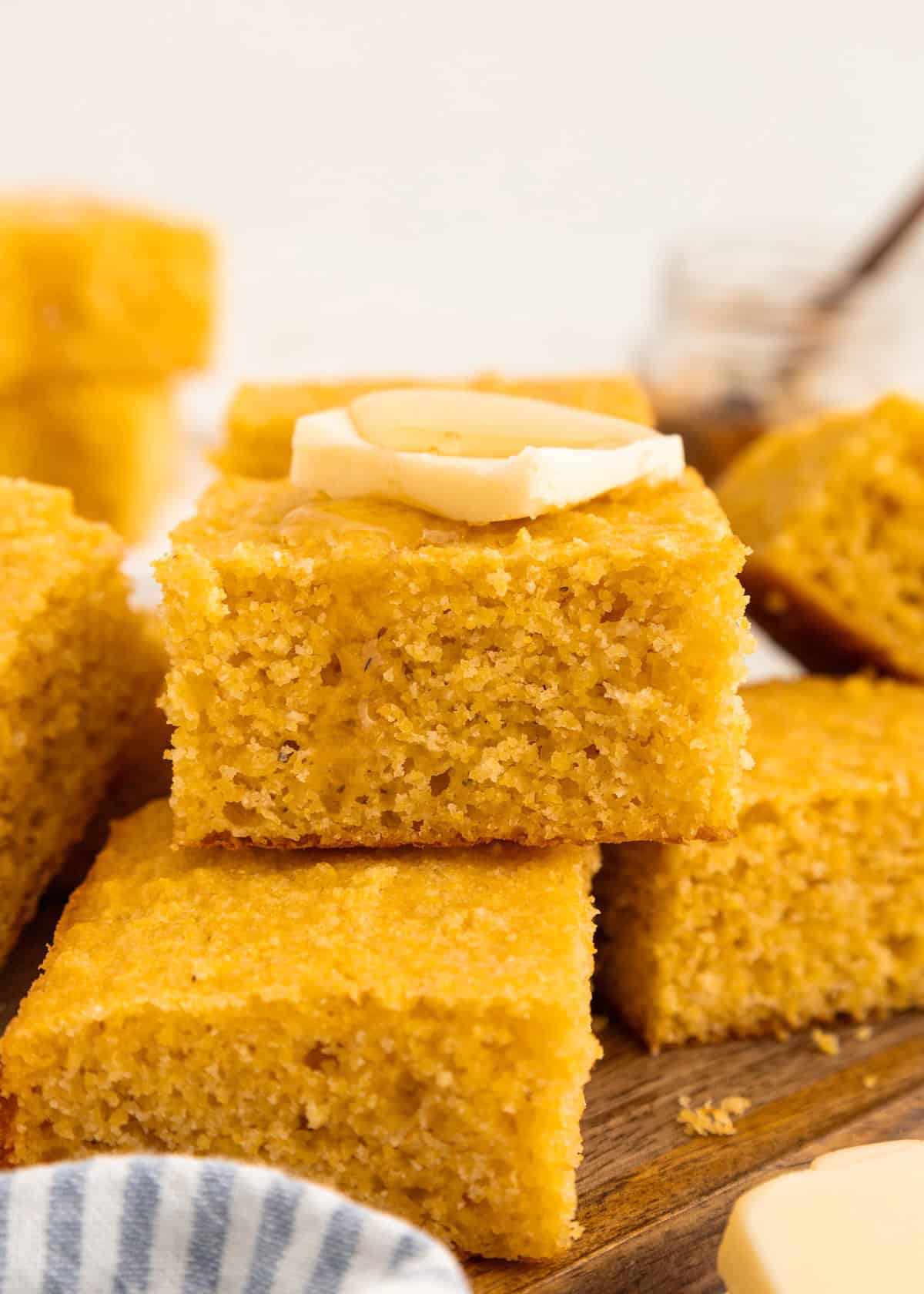 A square piece of cornbread topped with butter, stacked on other cornbread pieces.