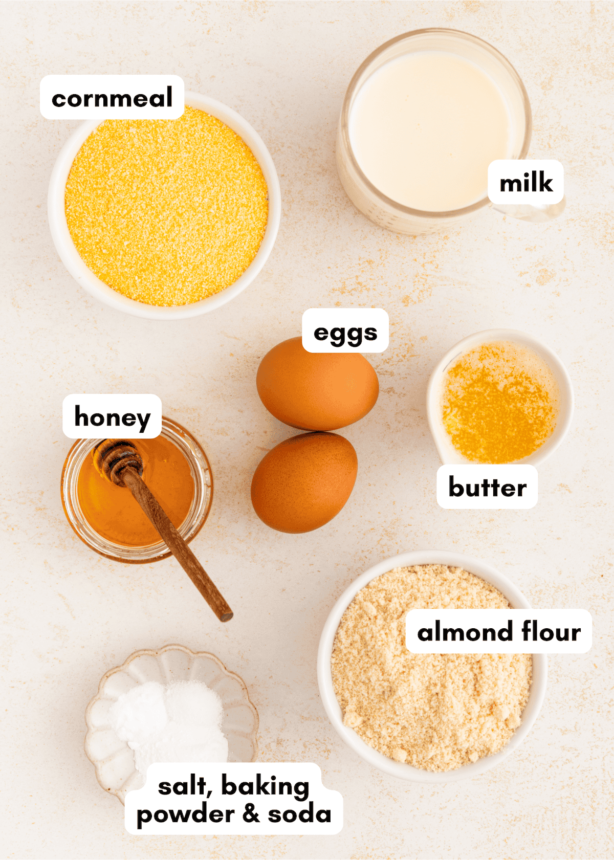 Bowls of cornmeal, milk, honey, butter, almond flour, eggs, and salt, baking powder & soda.