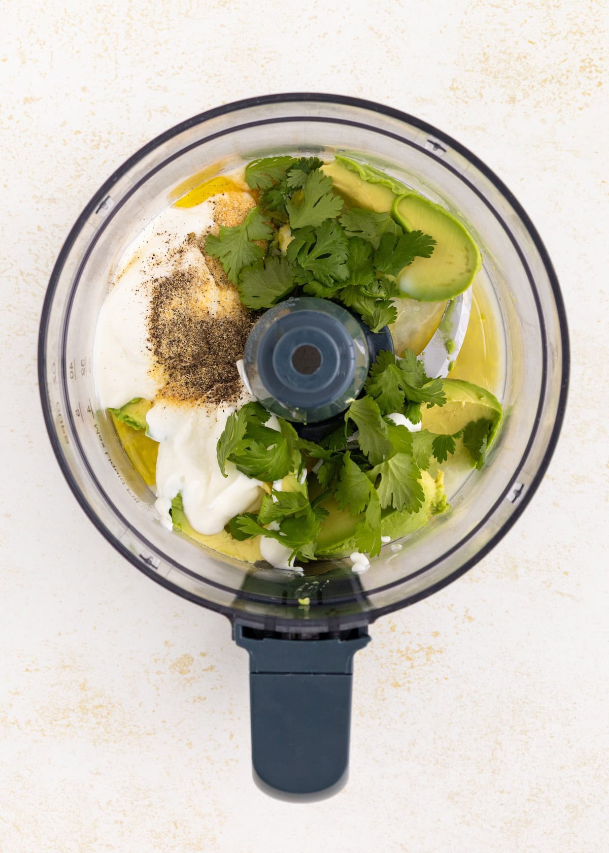 Food processor with avocado, cilantro, mayo, and spices for avocado lime ranch dressing.