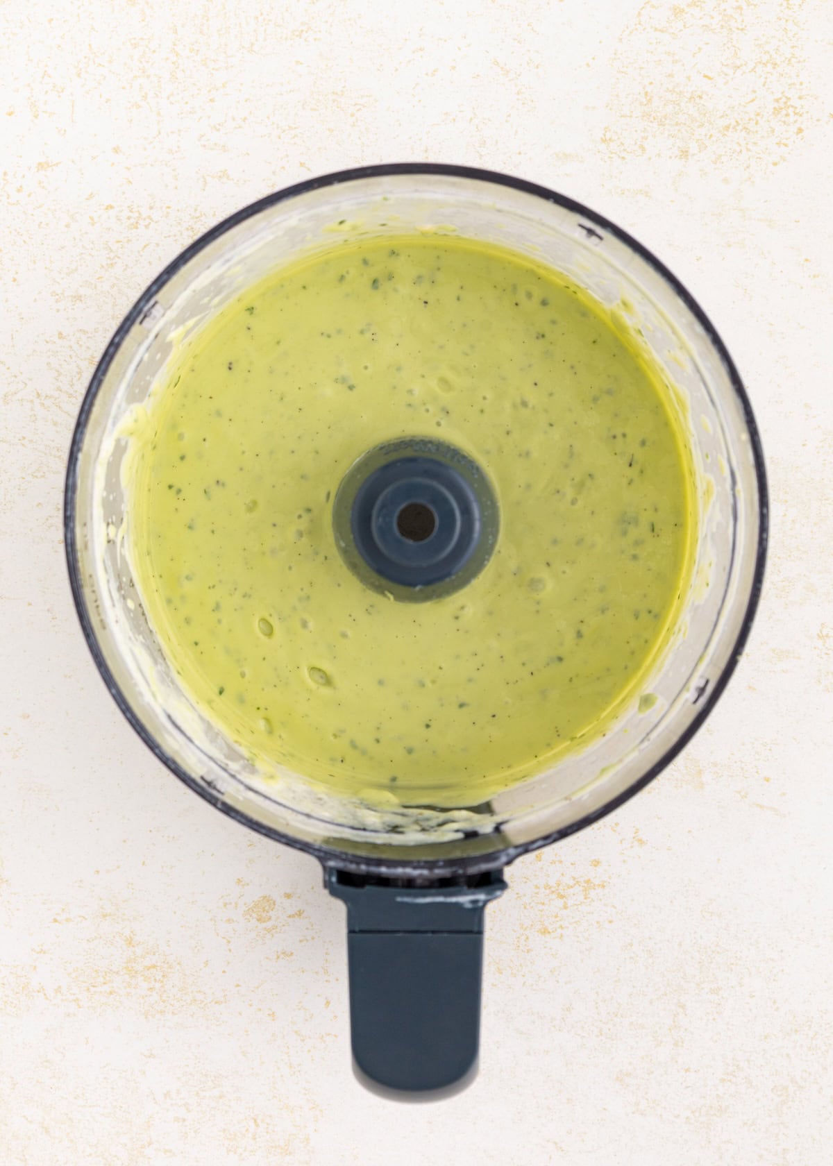 A food processor bowl filled with creamy avocado lime ranch dressing, viewed from above.