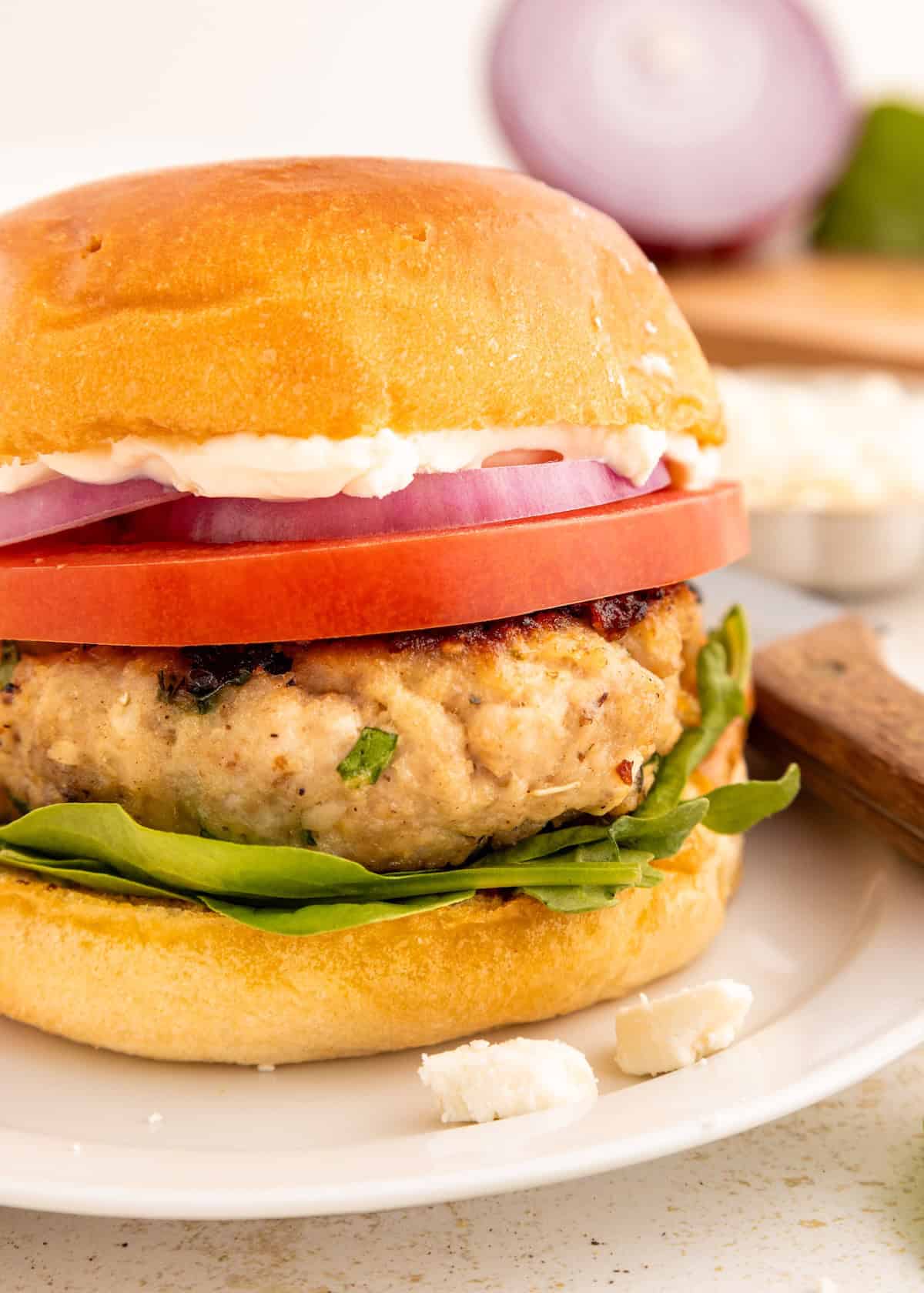Turkey burger with spinach, tomato, red onion, and mayo on a bun, served on a white plate.
