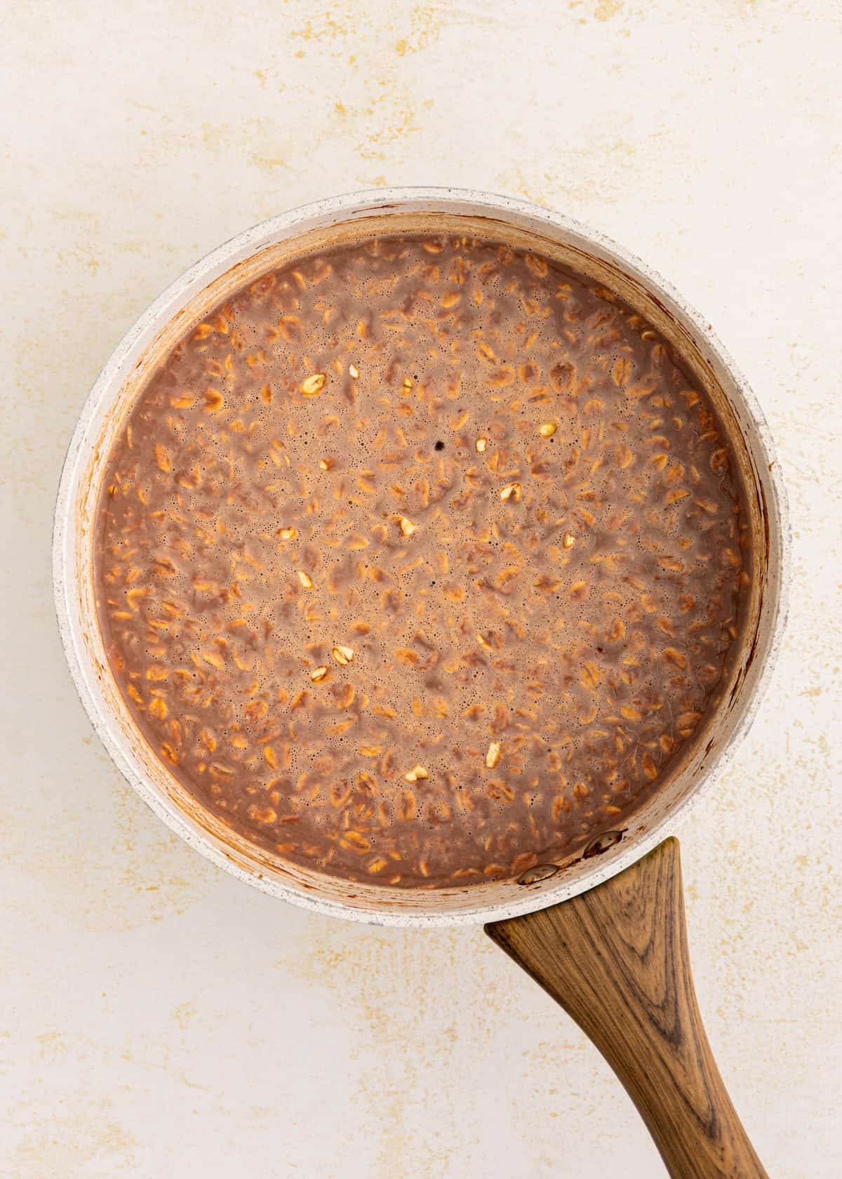 A saucepan of chocolate oatmeal with a wooden handle on a light background.