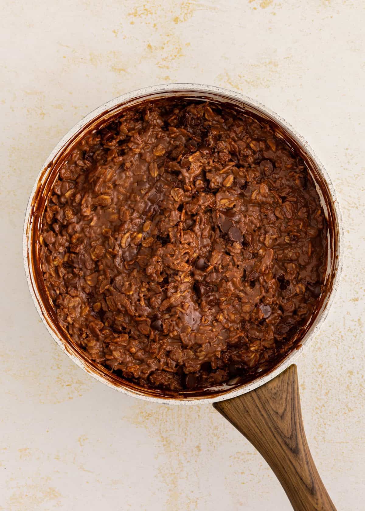 A saucepan filled with chocolate oatmeal on a light textured surface.