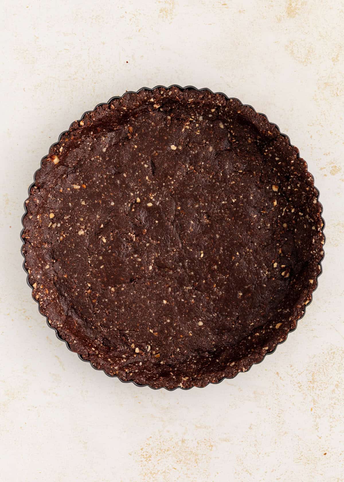 Chocolate crust pressed into a round tart pan on a light surface.