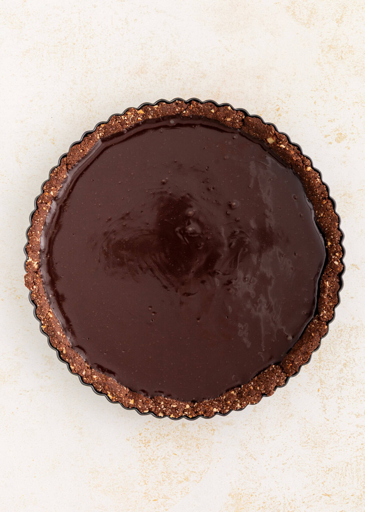 A chocolate tart with a glossy filling and a crumbly crust on a light surface.
