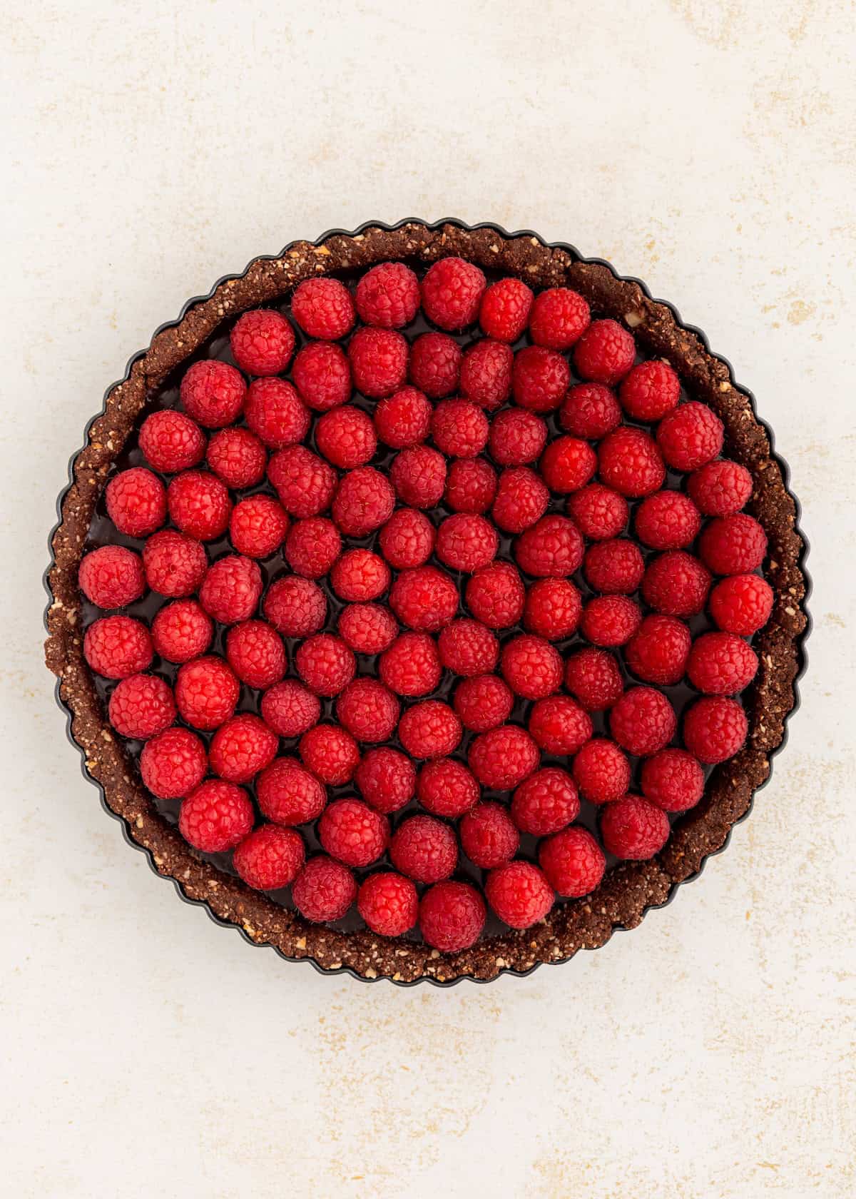 Chocolate tart topped with evenly arranged fresh raspberries on a light background.