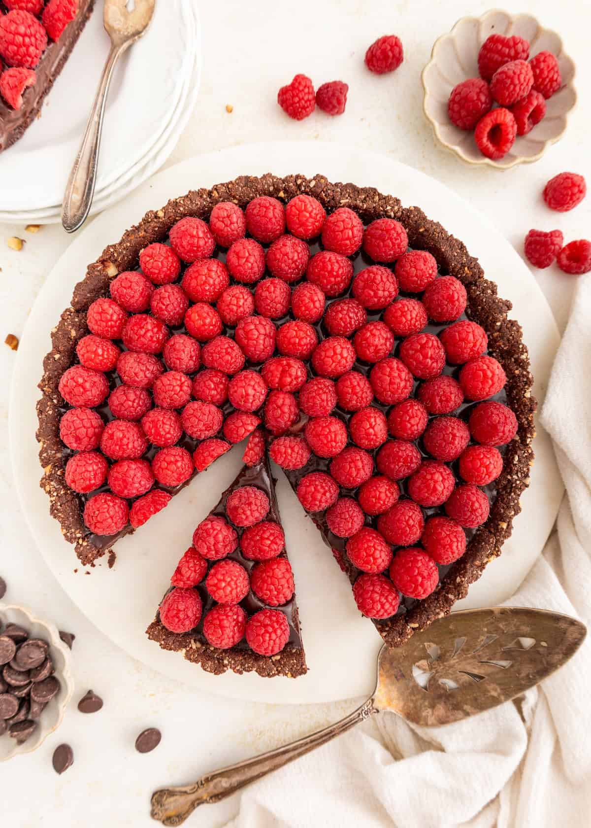 A chocolate tart topped with fresh raspberries, with one slice pulled out.