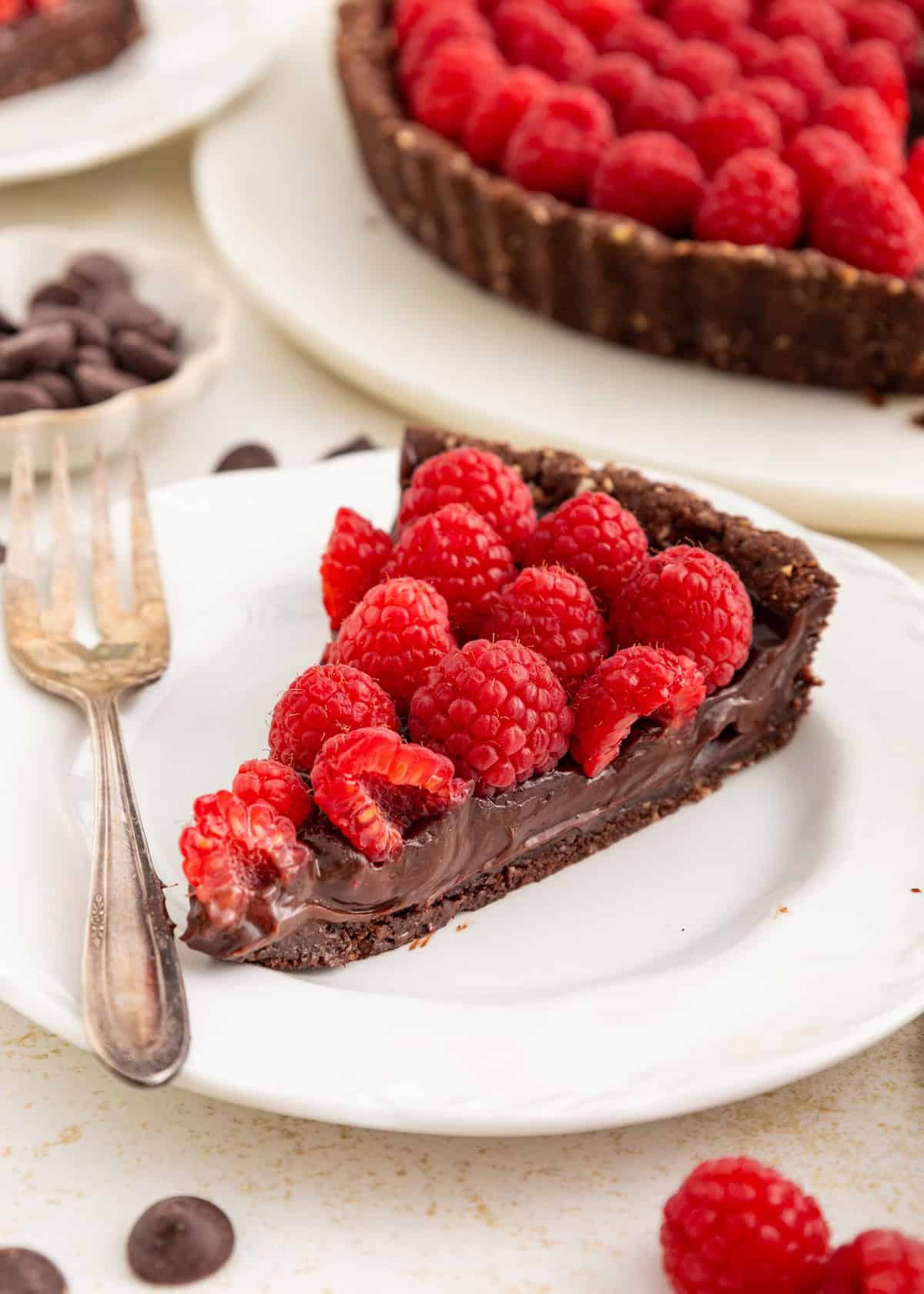 A slice of chocolate tart topped with fresh raspberries on a white plate with a fork.