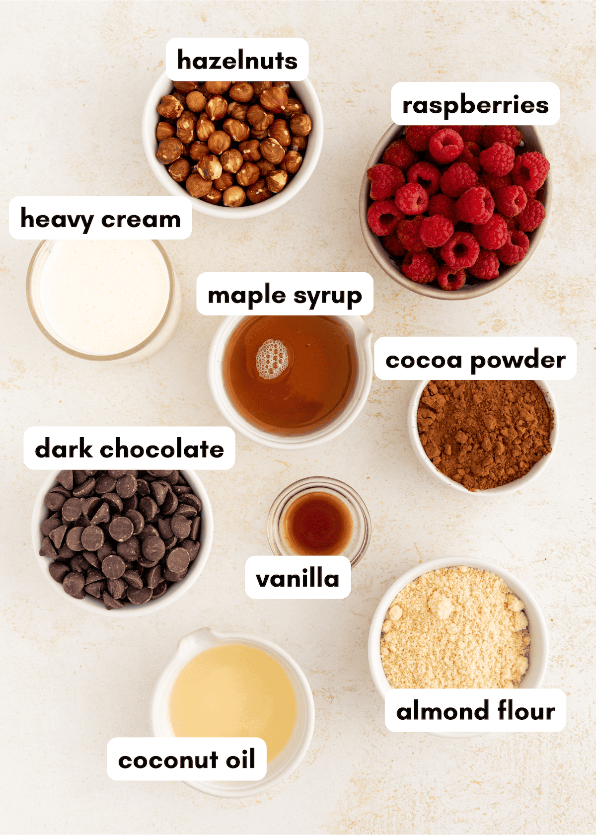 Bowls with hazelnuts, raspberries, cream, syrup, cocoa, chocolate, vanilla, flour, and coconut oil.