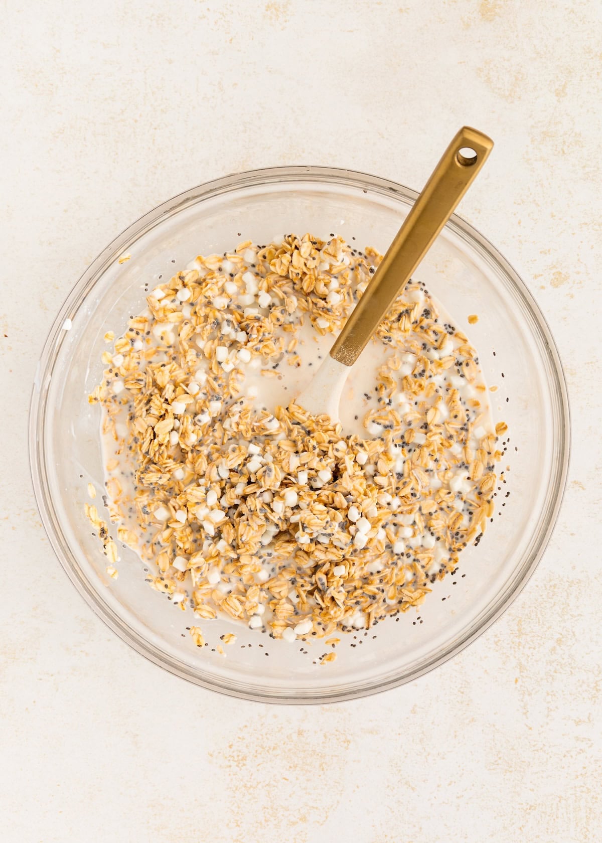 A bowl of oats, chia seeds, and milk with a spoon on a light surface.