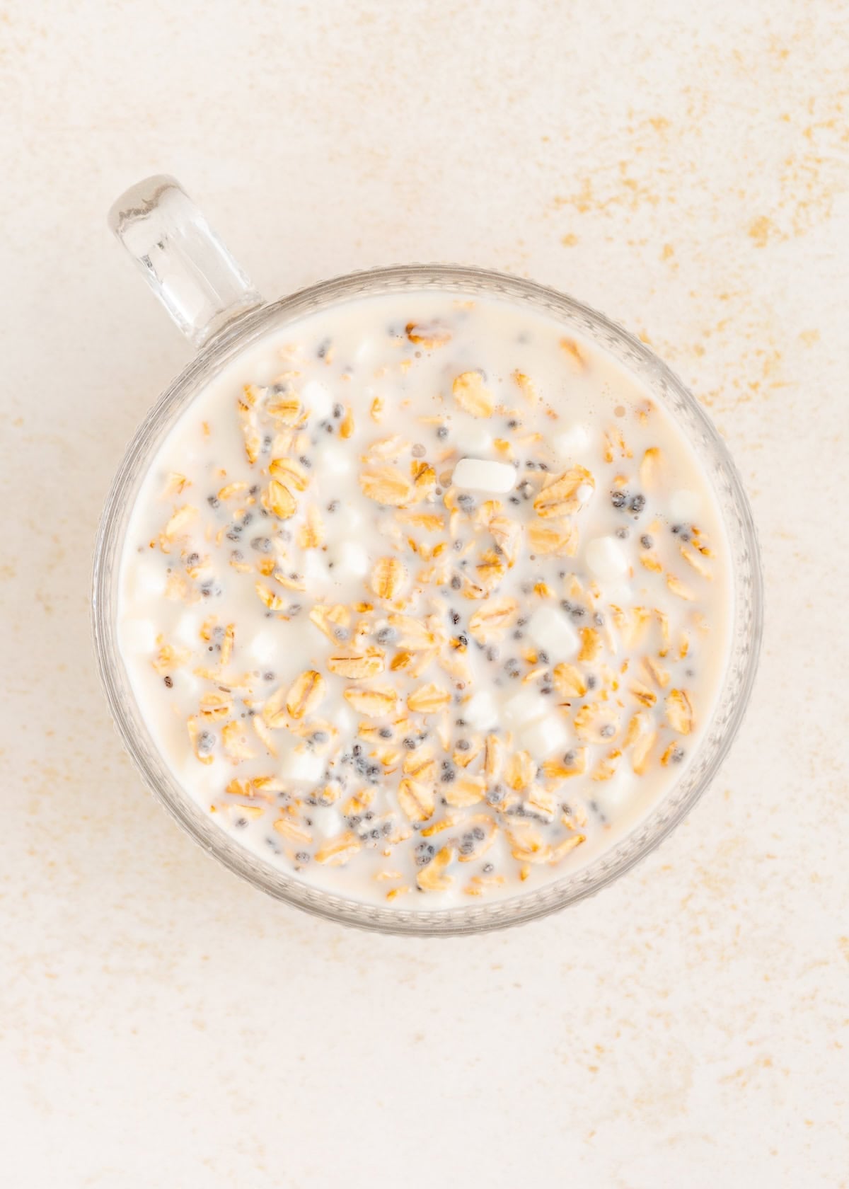 A glass cup of overnight oats with milk and chia seeds viewed from above.