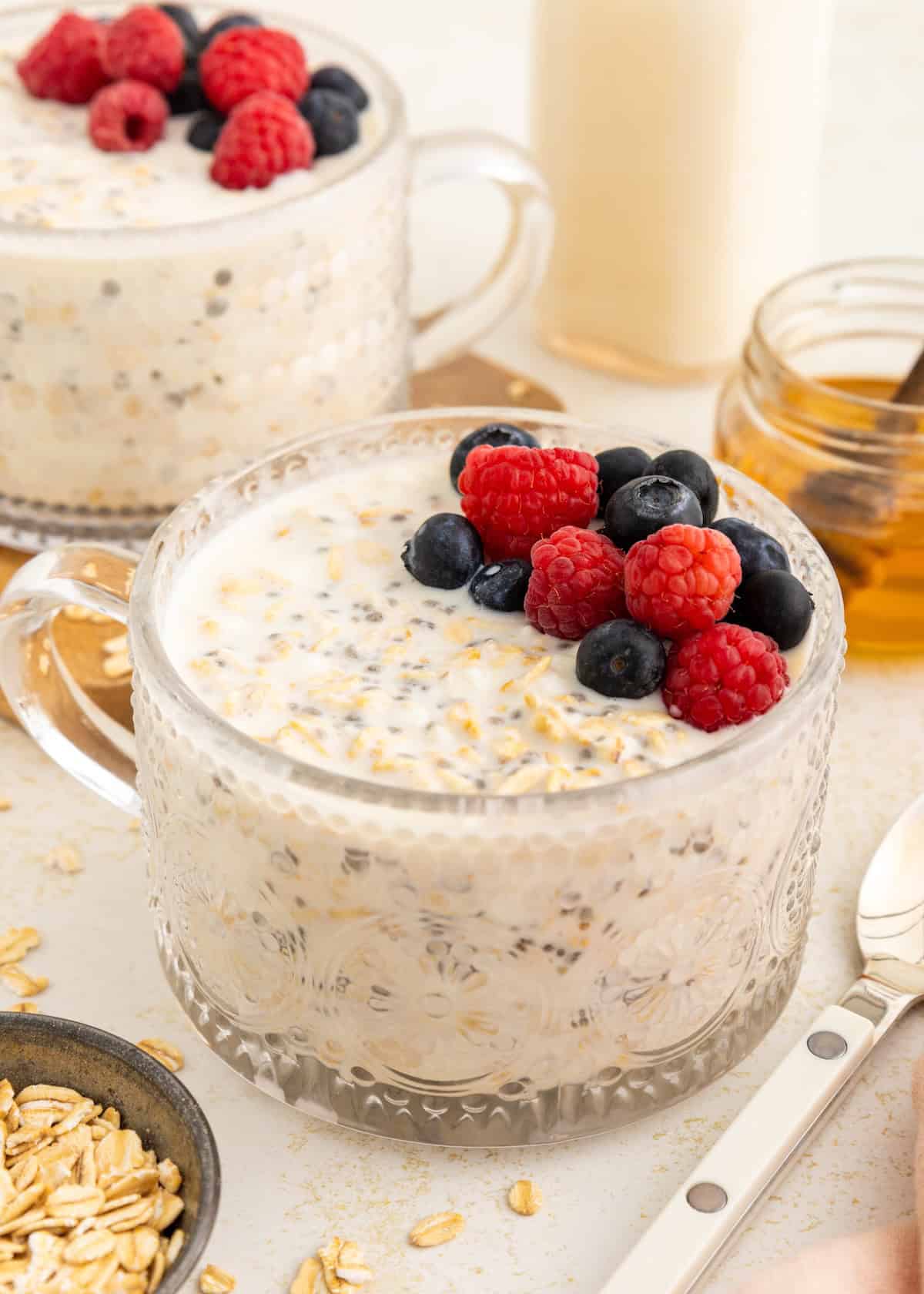 A glass cup of overnight oats topped with raspberries and blueberries on a table.