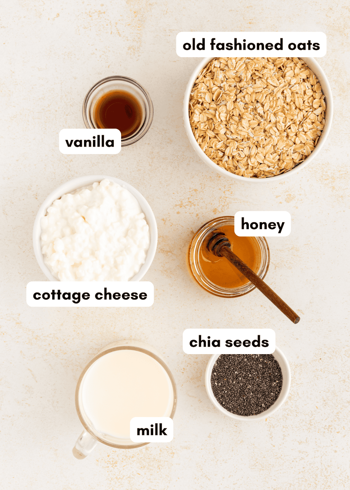 Bowls of cottage cheese overnight oats, chia seeds, honey, milk, and vanilla on a light surface.