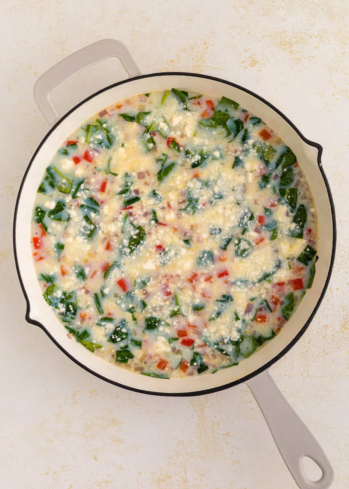 A skillet filled with an uncooked vegetable and cheese egg mixture, ready to be baked.