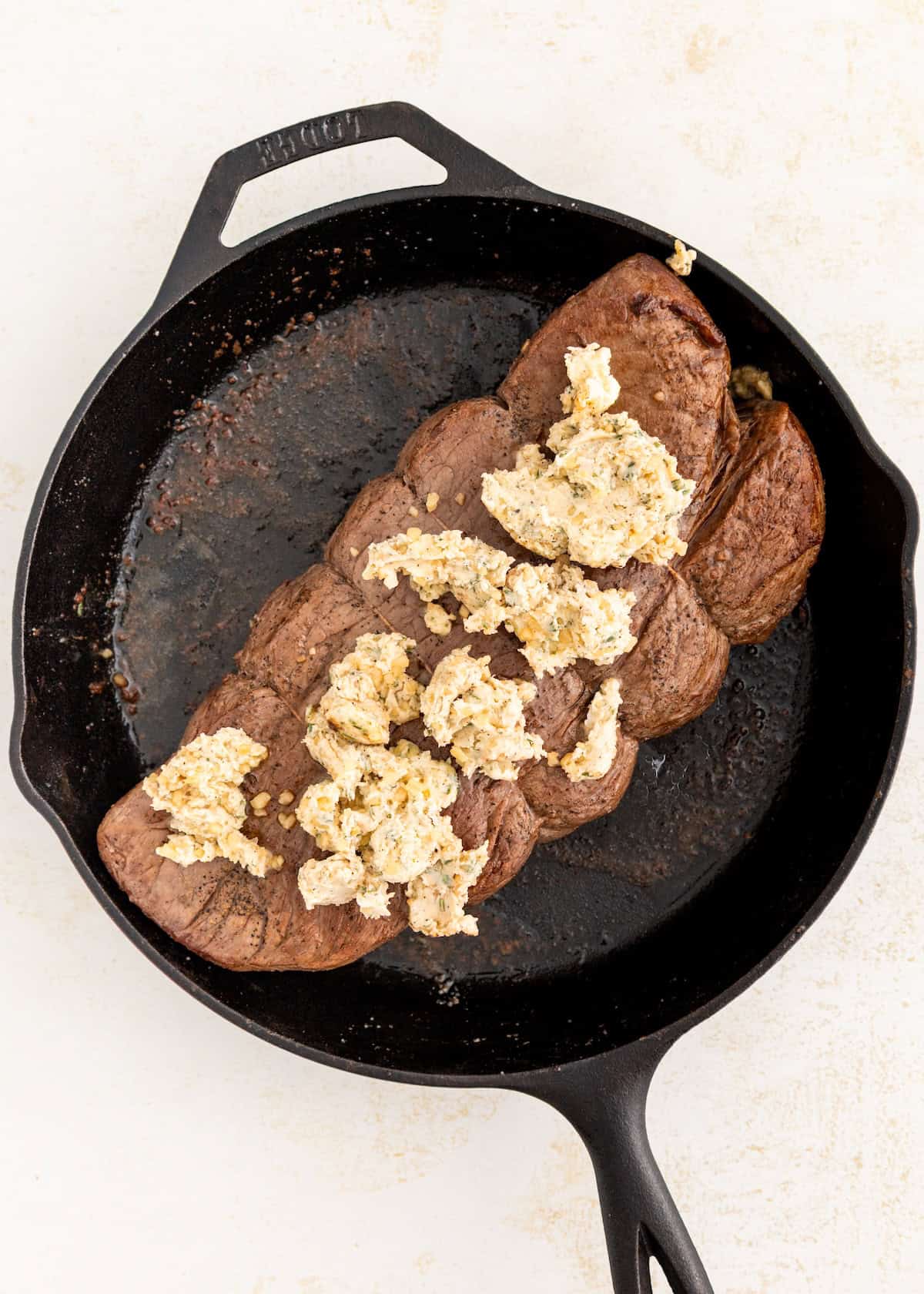 A garlic herb roast beef tenderloin in a cast iron skillet topped with herbed butter.
