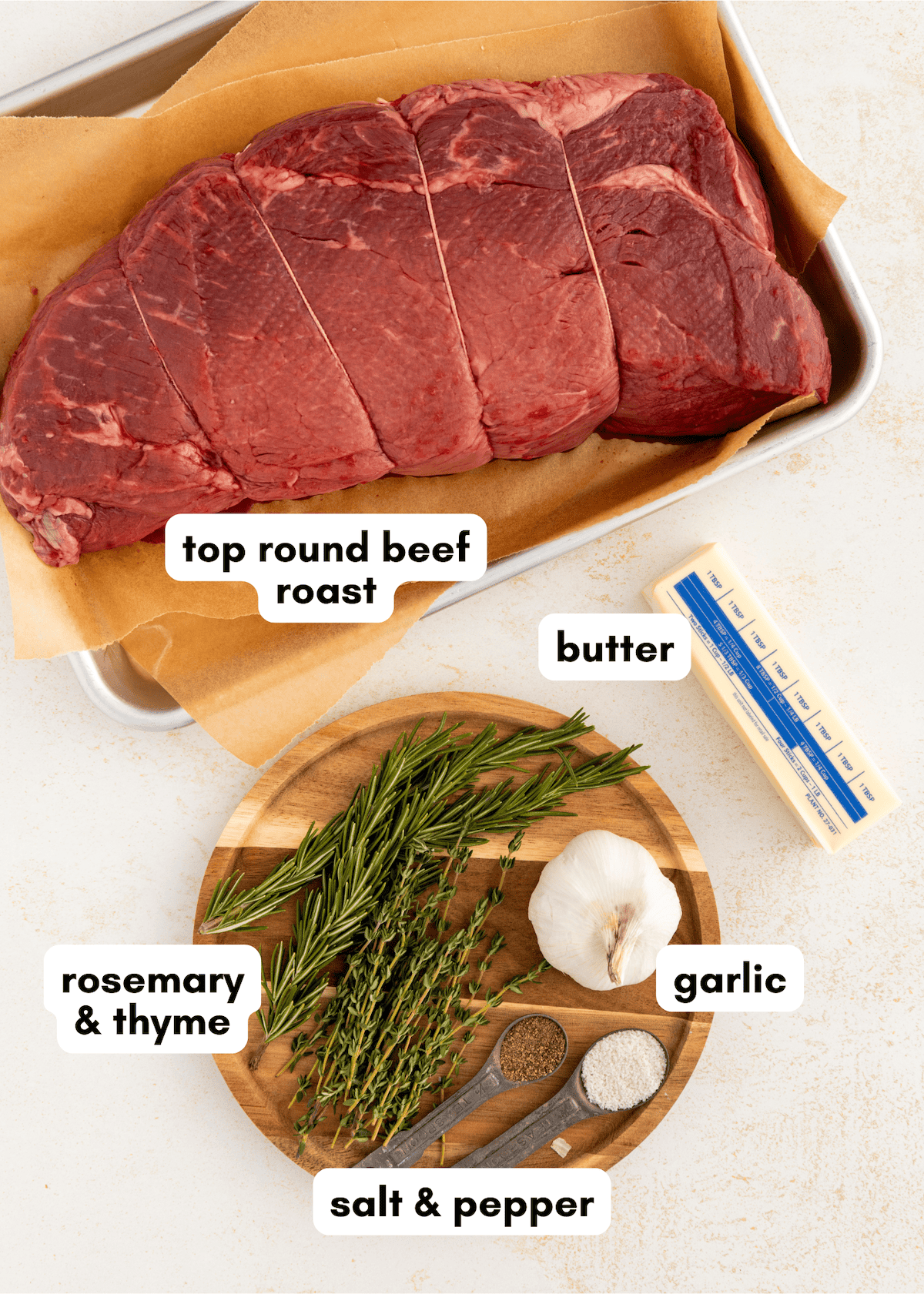 Garlic herb roast beef, butter, rosemary, thyme, salt, and pepper arranged on a table.